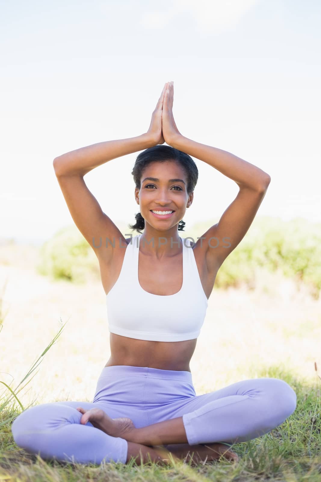 Fit woman sitting on grass in lotus pose smiling at camera on a sunny day in the countryside