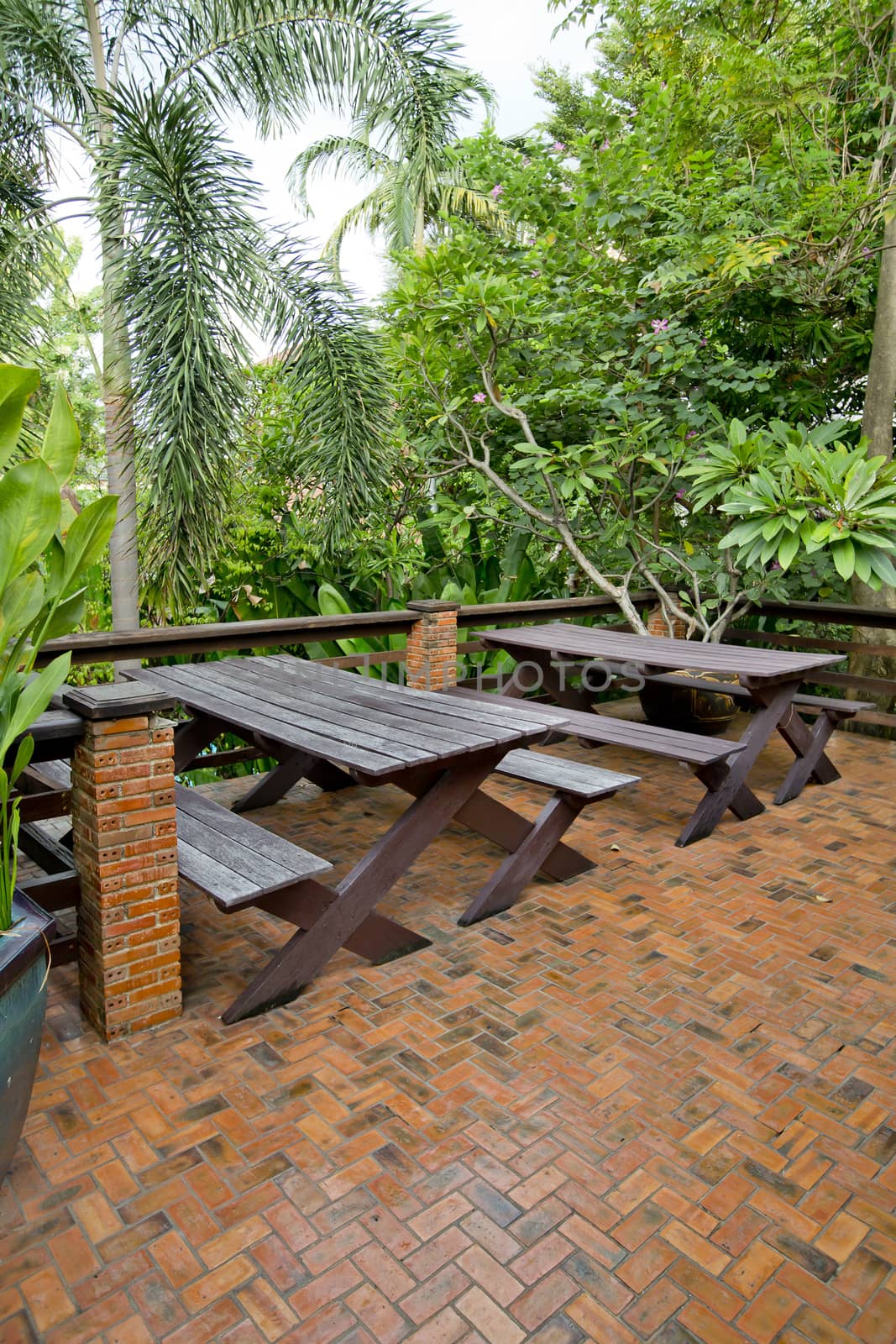 Wooden chairs and table set at balcony in a green plant garden.