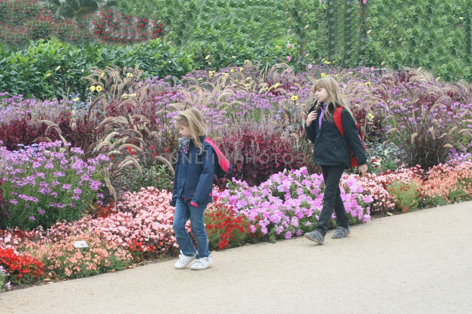 two blonde girls and colorful flower beds