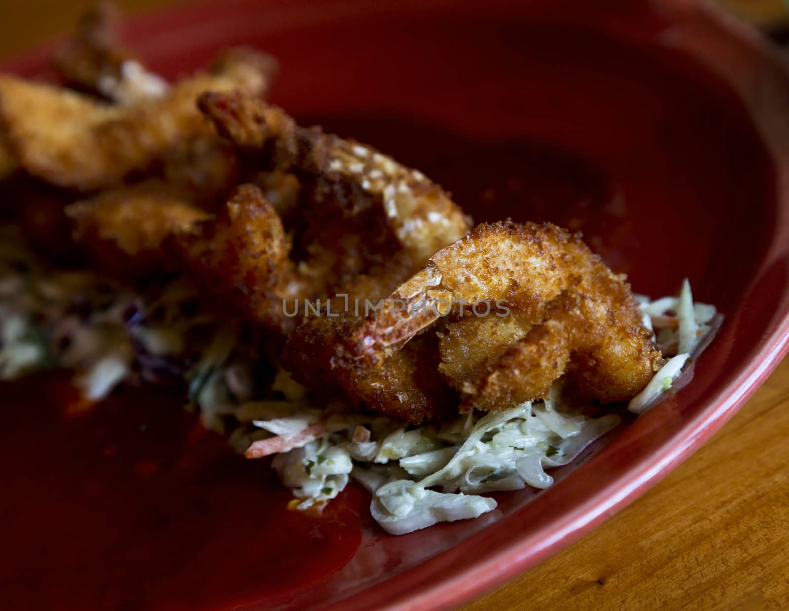 Crispy fried shrimp placed atop shredded cabbage  on red plate. Wood grain table is rustic.  Red plate reflects modern Southwestern cuisine style.