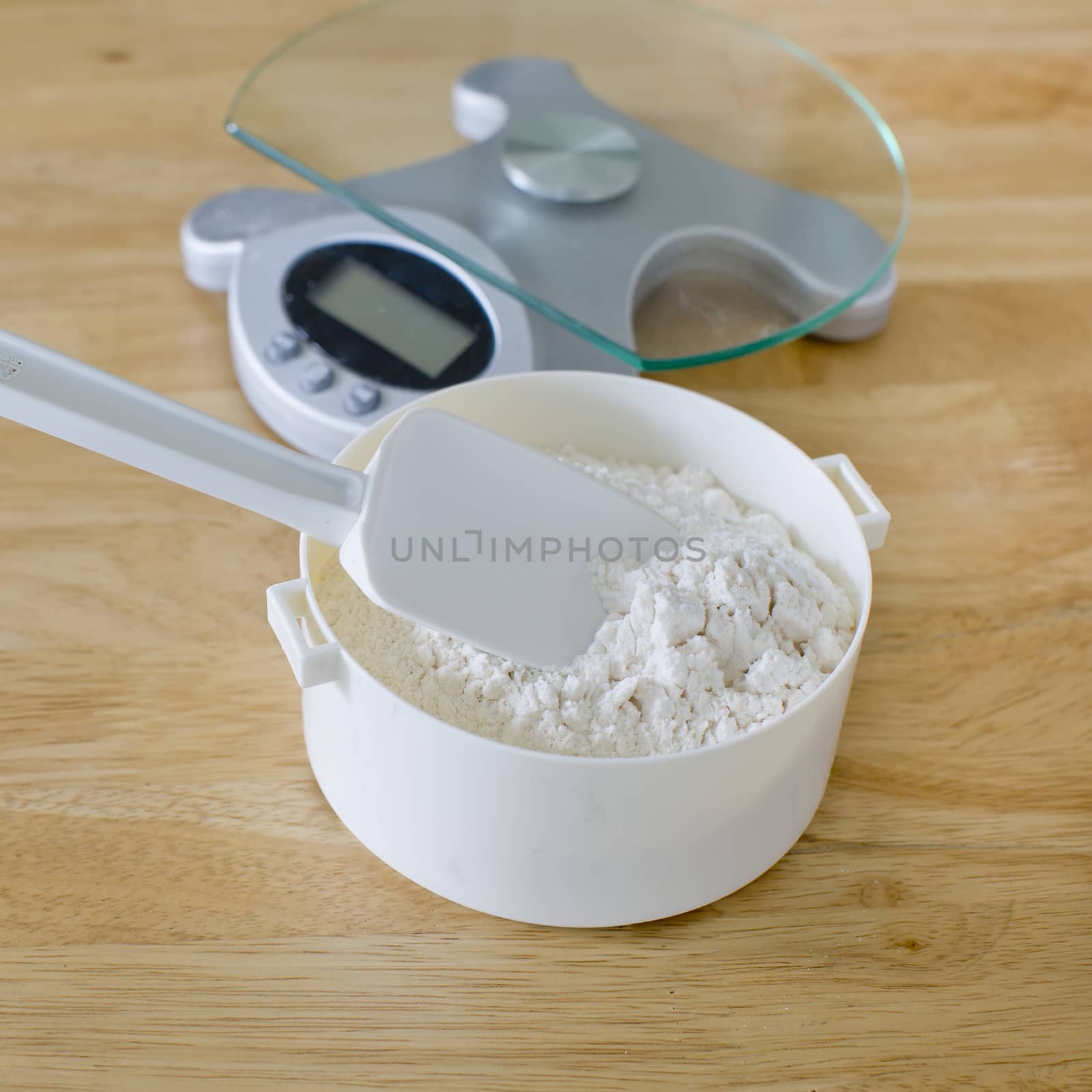 Bread flour in white bowl with rubber scraper and scale on wood table ready to baking bread