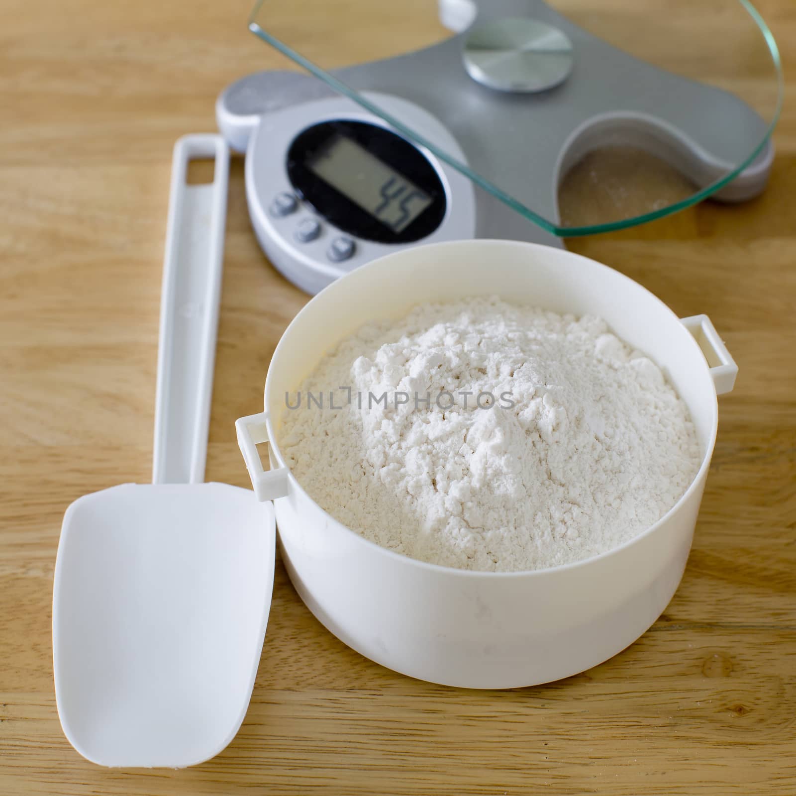 Bread flour in white bowl with rubber scraper and scale on wood table ready to baking bread