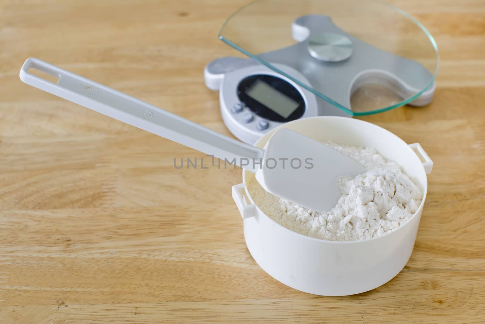 Bread flour in white bowl with rubber scraper and scale on wood table ready to baking bread