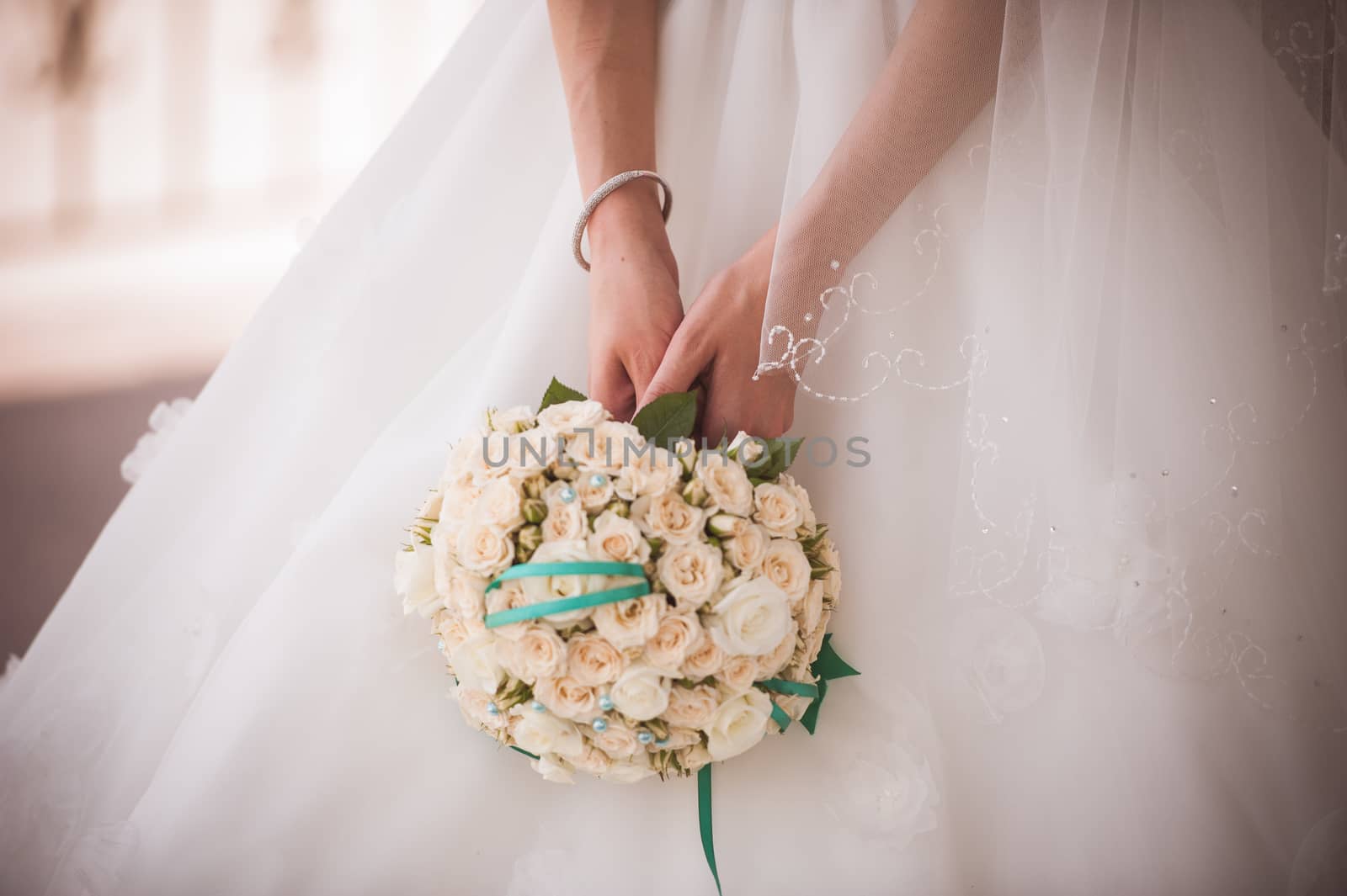 bride holding wedding bouquet from white roses with green ribbon