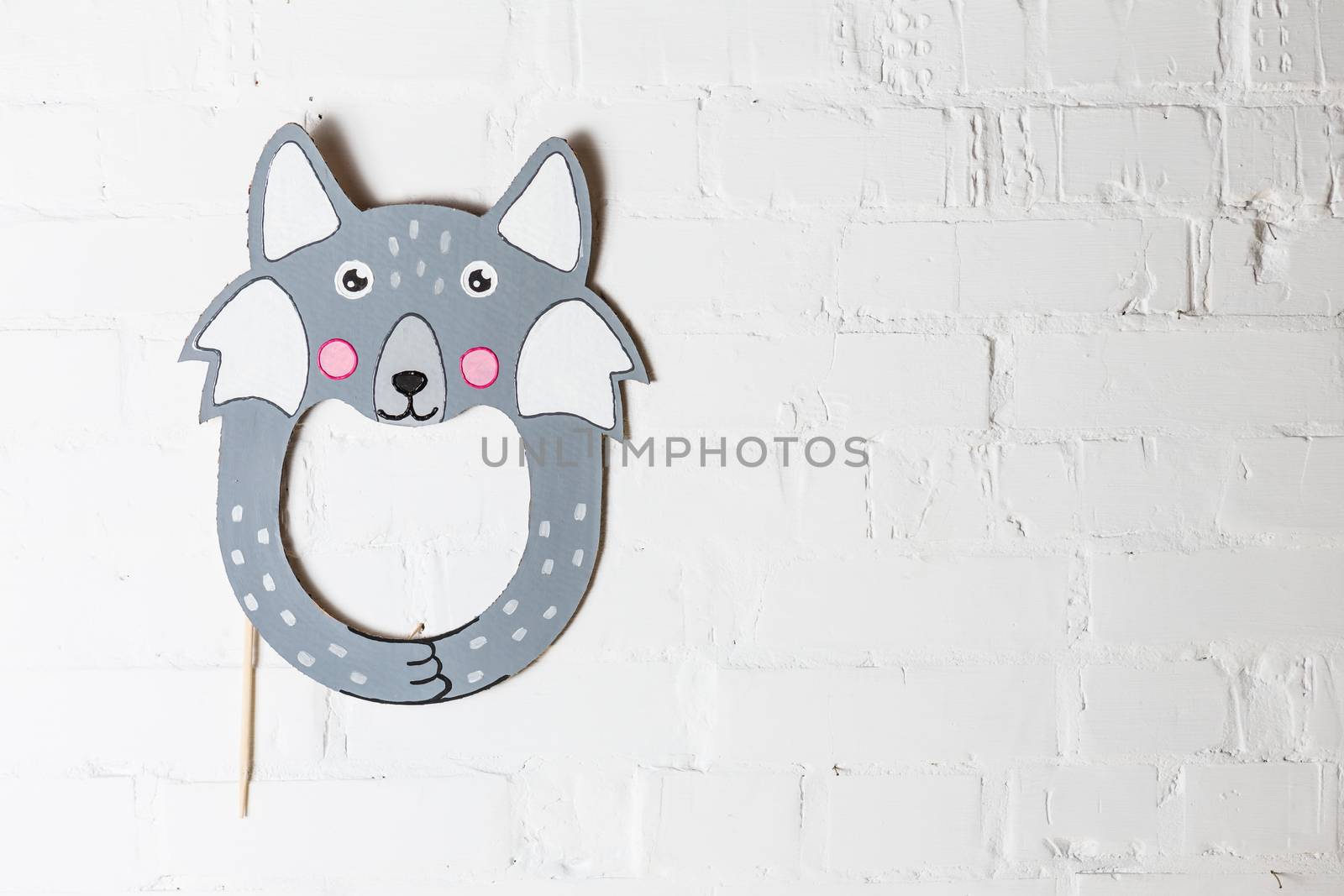 Bright cardboard mask on a white brick wall.  by sarymsakov