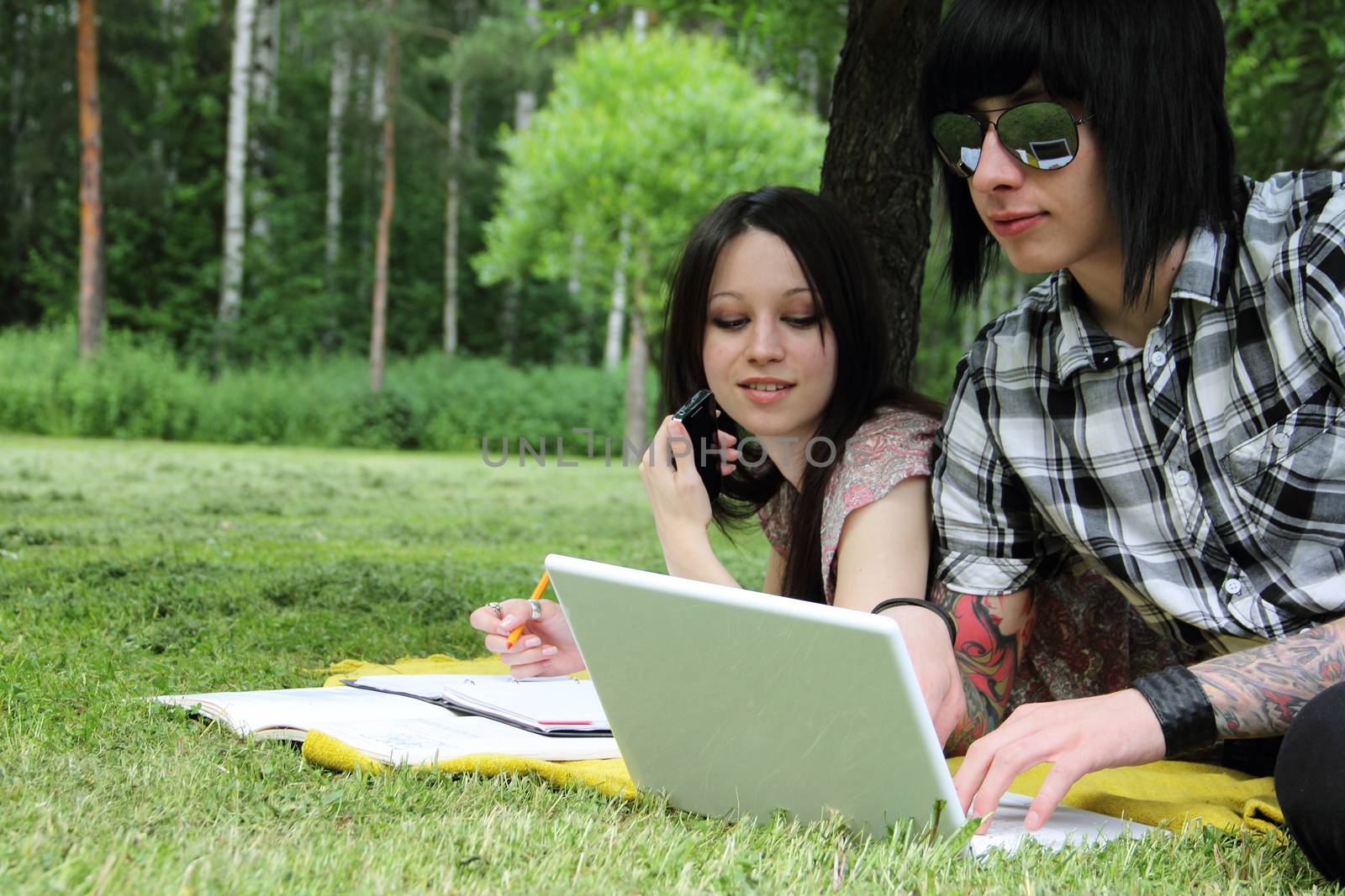 Couple of young students studying outdoors with laptop and books