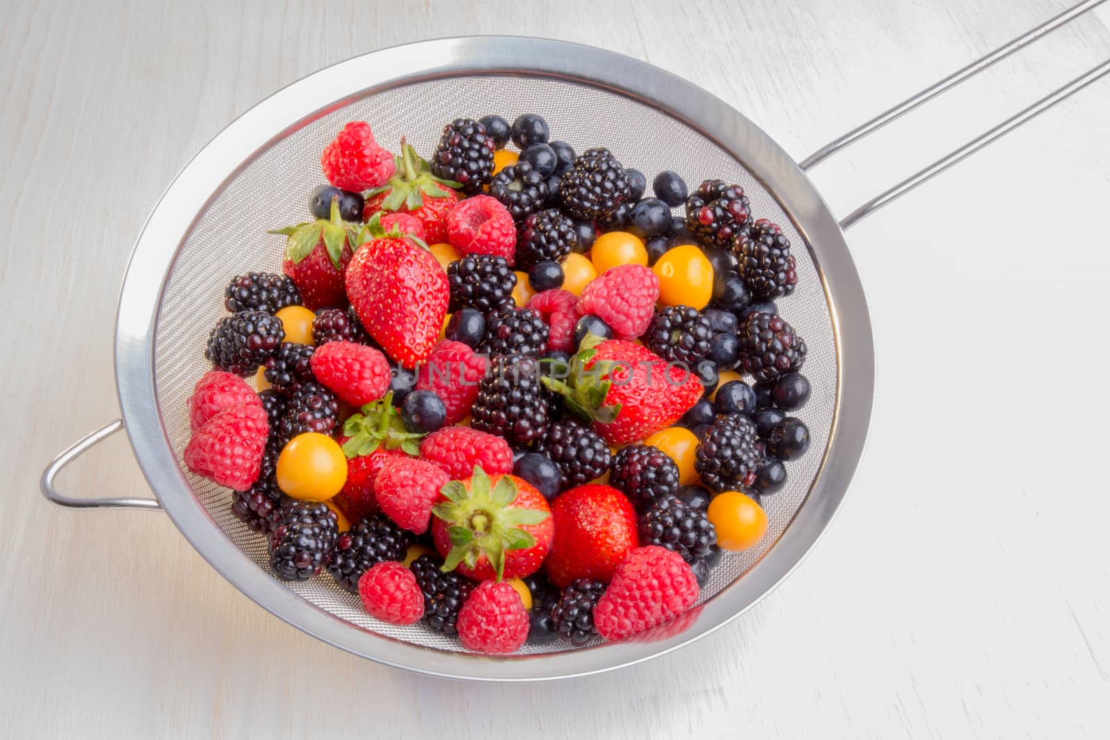 Mixed berries of different types, colors, and shapes in a colander.