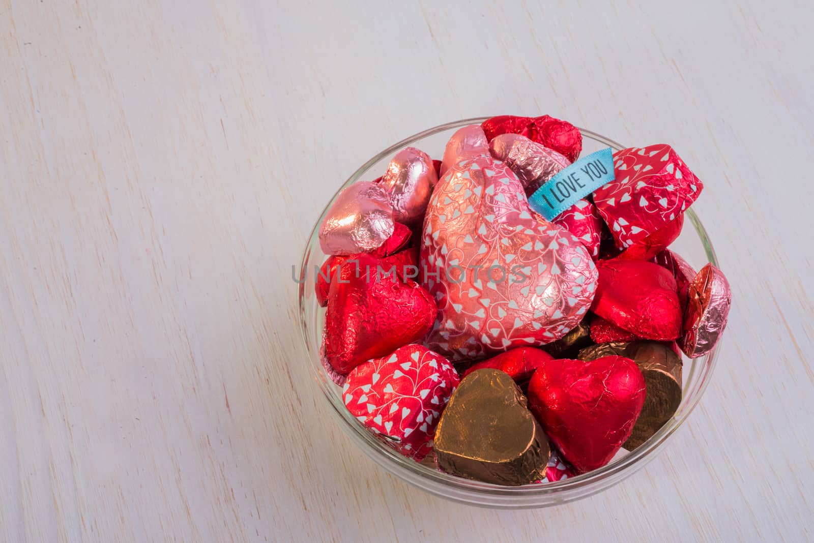 A glass bowl filled with heart shaped chocolates.