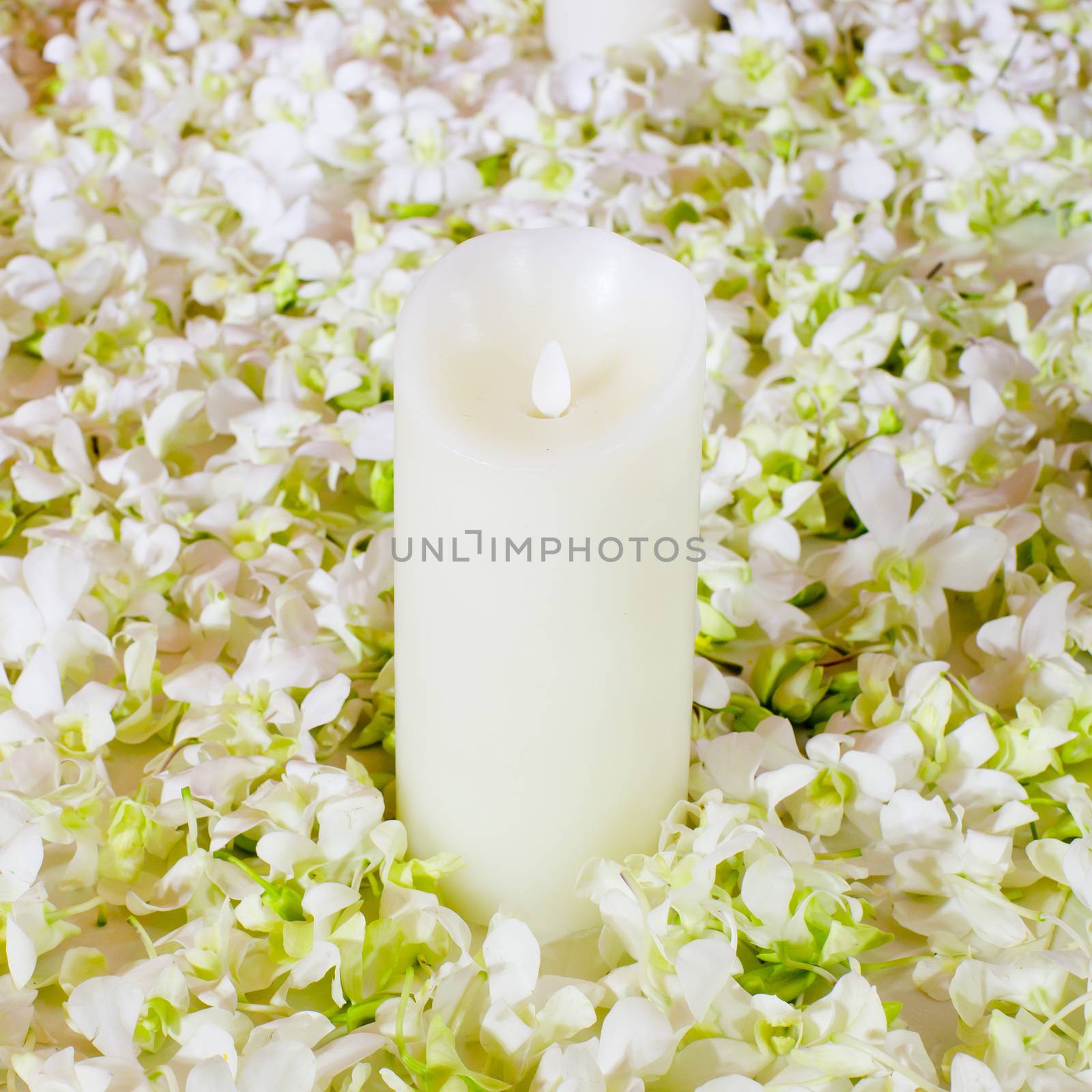 The big white candle in a wreath from artificial flowers. A wedding composition, an ornament