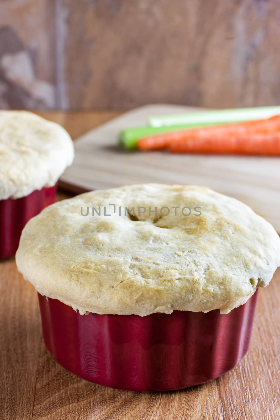 Chicken pot pie in a red ramakin cools on a wooden counter top in the afternoon sun.