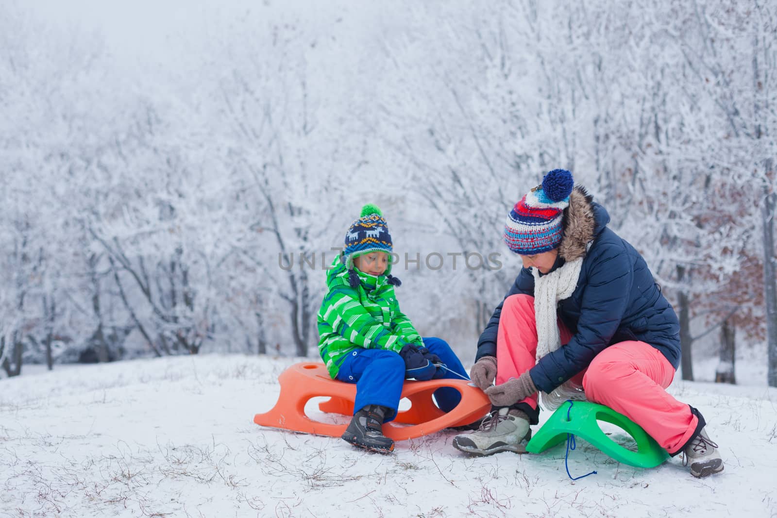 Winter, play, fun - Mother and her cute little son having fun with sled in winter park