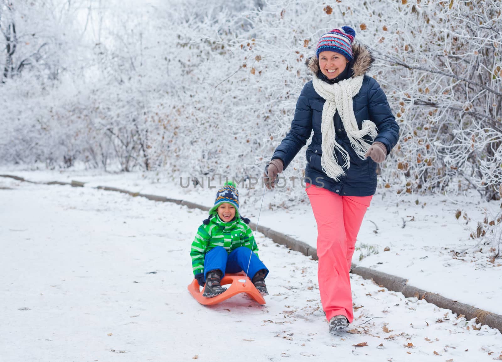 Winter, play, fun - Mother and her cute little son having fun with sled in winter park