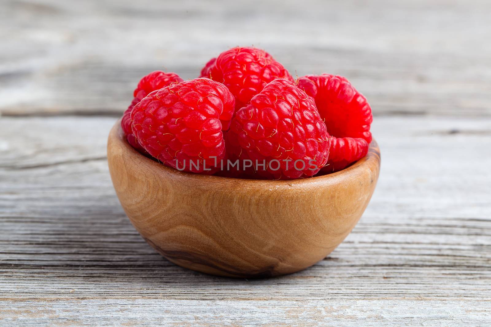 raspberries in wooden bowl, on wooden background by motorolka