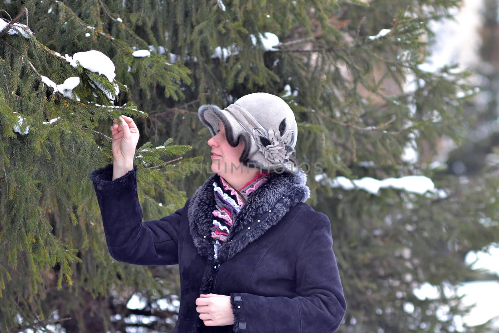 The woman in a hat and a sheepskin coat costs near a fir-tree in park