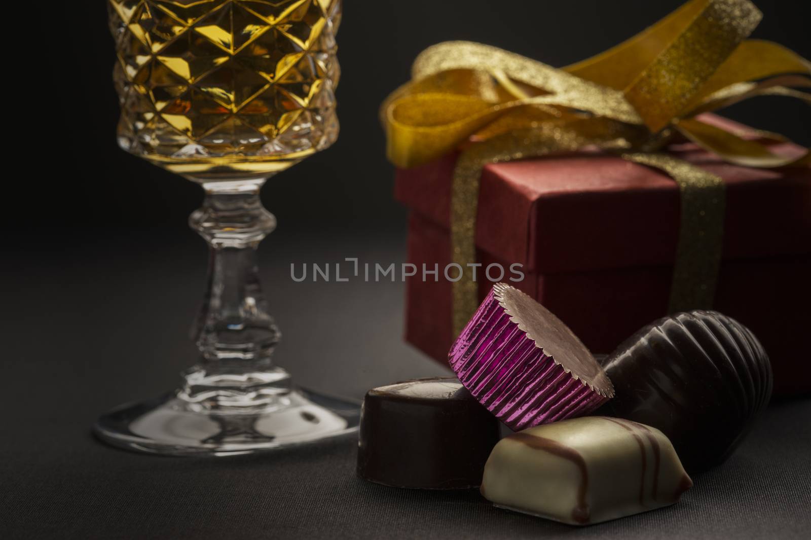 Close up of a cluster of delicious handmade luxury chocolates with a goblet of white wine and a gift with golden bow in a concept of a romantic anniversary, Christmas or Valentines day