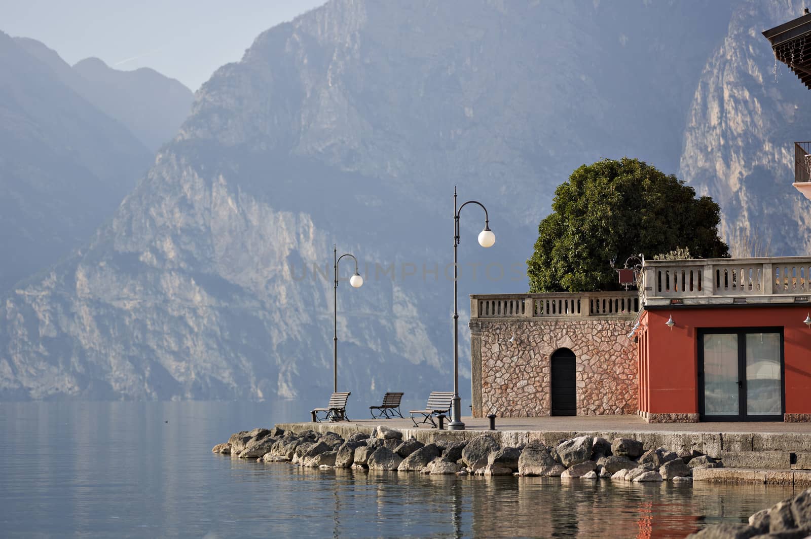 Three pews by the shore of Lake Garda in the northern Italy surrounded by mountains and water.
