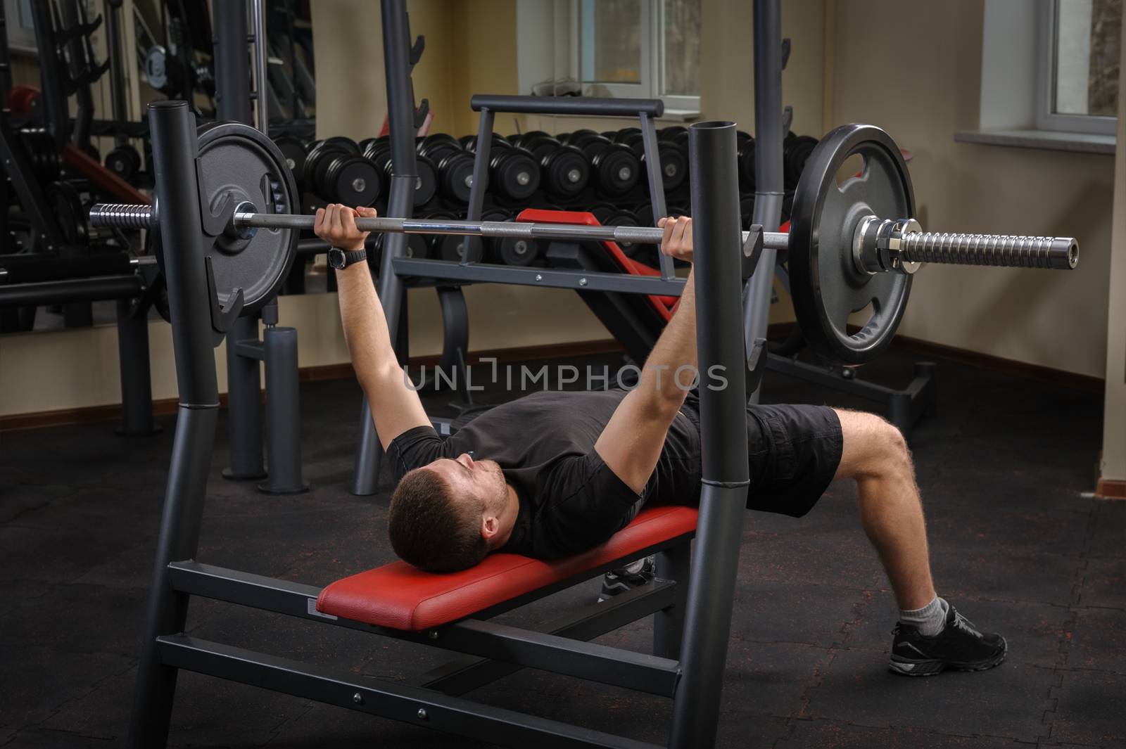 young man doing bench press workout in gym by starush