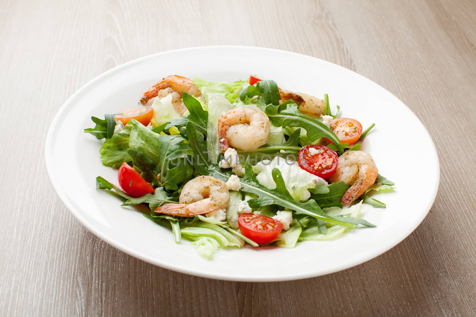 Fresh gourmet seafood salad with lettuce, rocket and corn greens, shrimps, cherry tomatoes, cheese  served in white plate