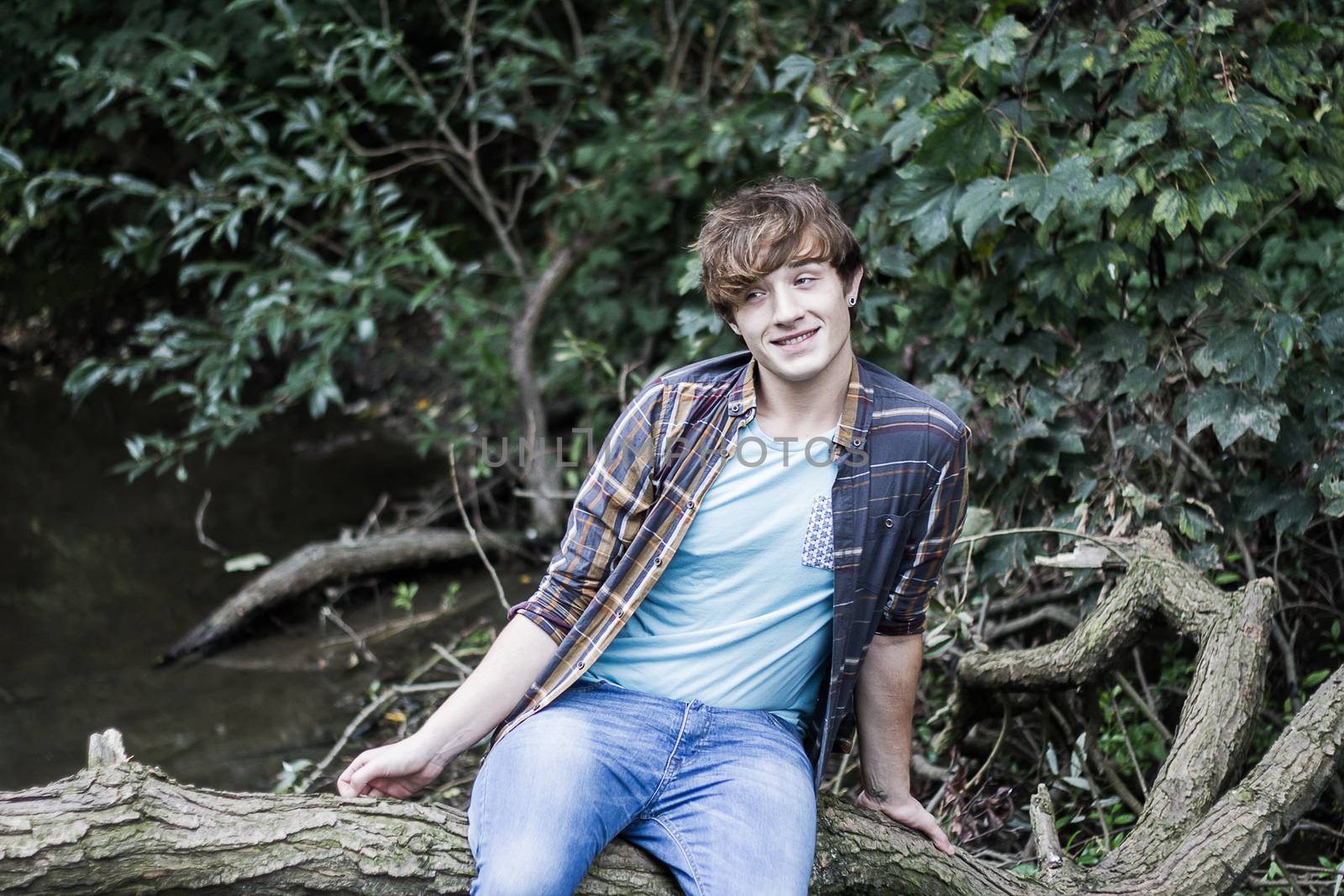 portrait of young man sitting on branch over a stream