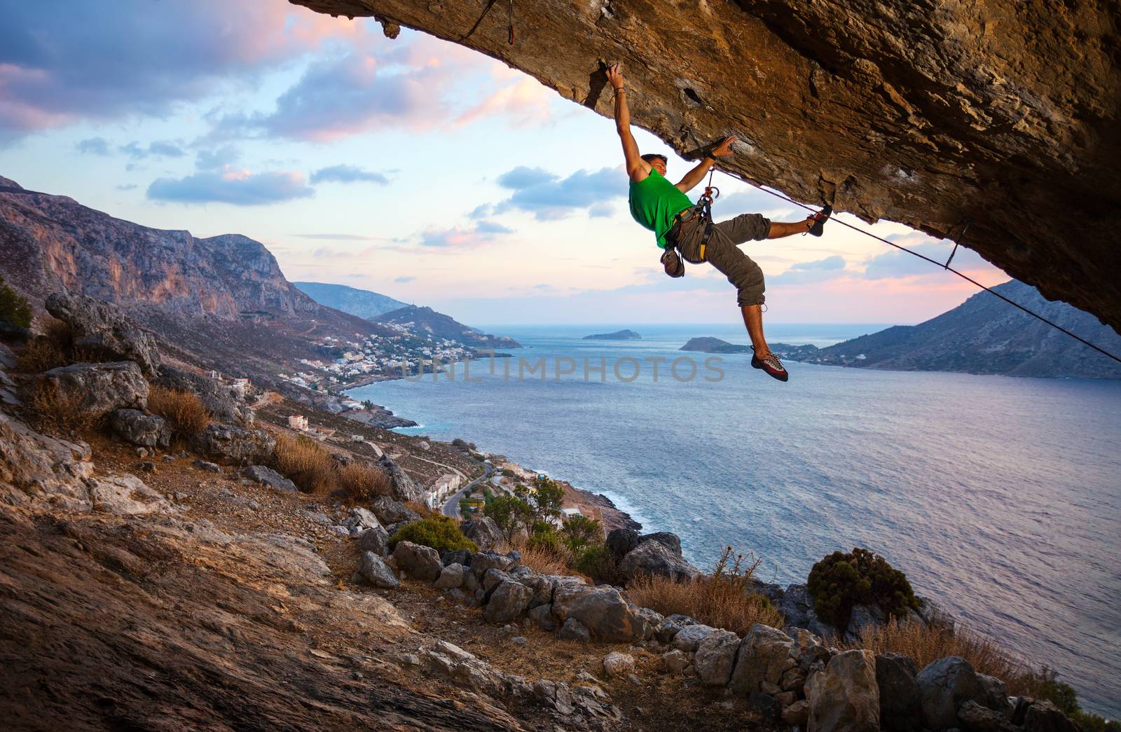 Male climber climbing overhanging rock against beautiful view of coast below