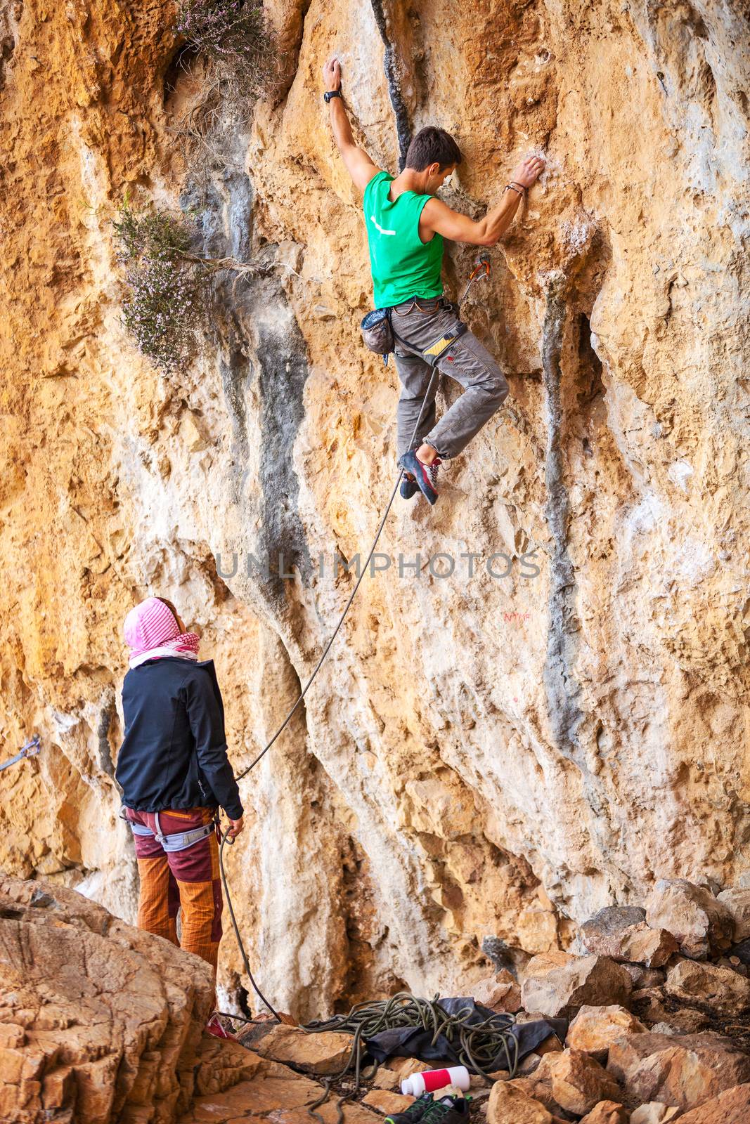 Man lead climbing on cliff, belayer watching hi by photobac