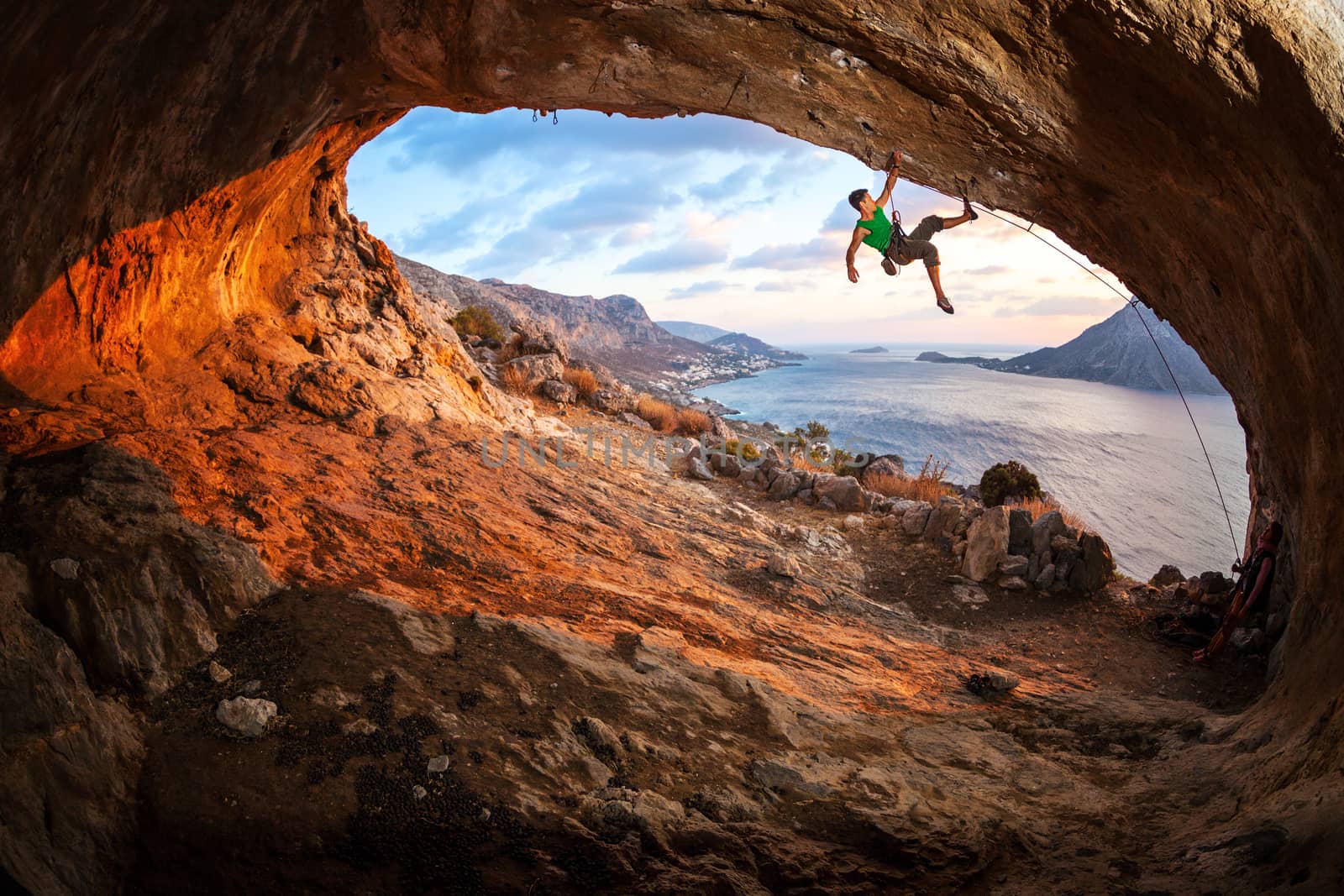 Male rock climber climbing along a roof in a cave at sunset