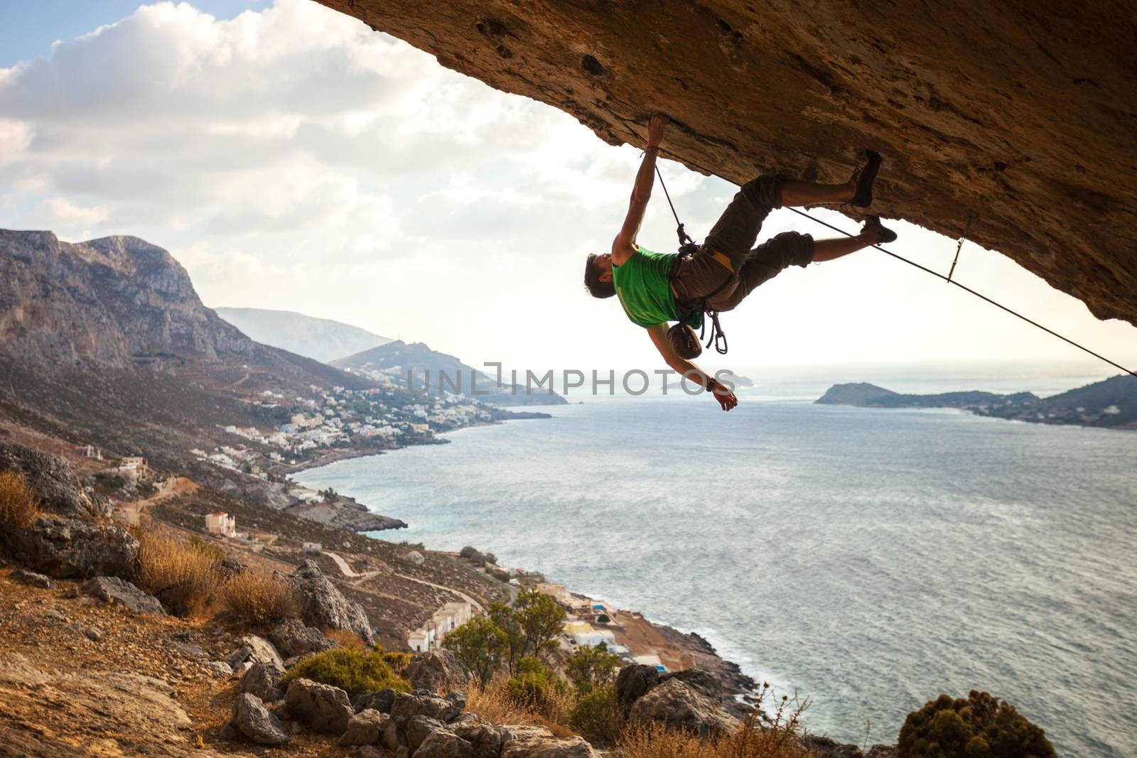 Male climber climbing overhanging rock against beautiful view of coast below