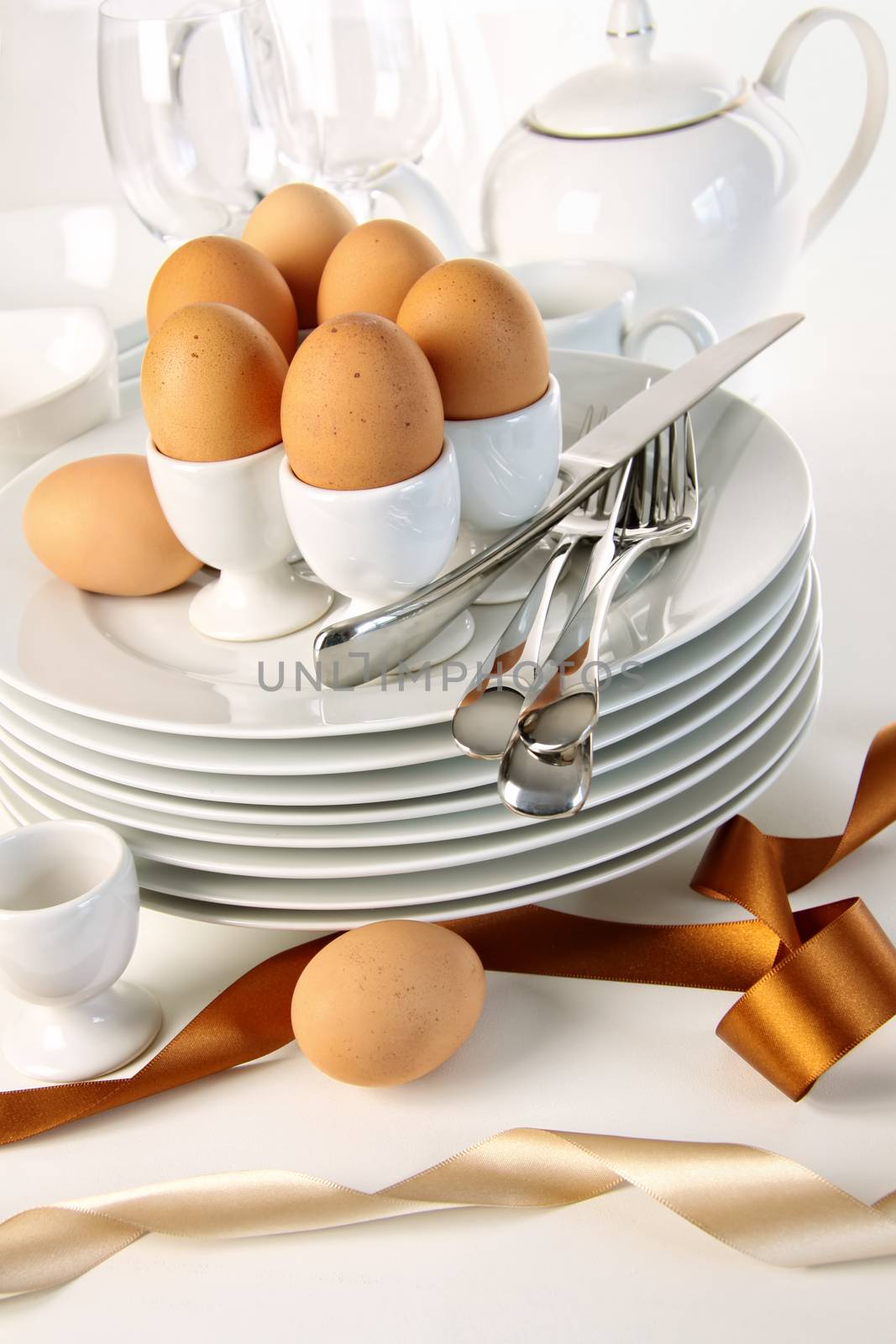 Eggs in white egg cups on a pile of plates with ribbons by Sandralise