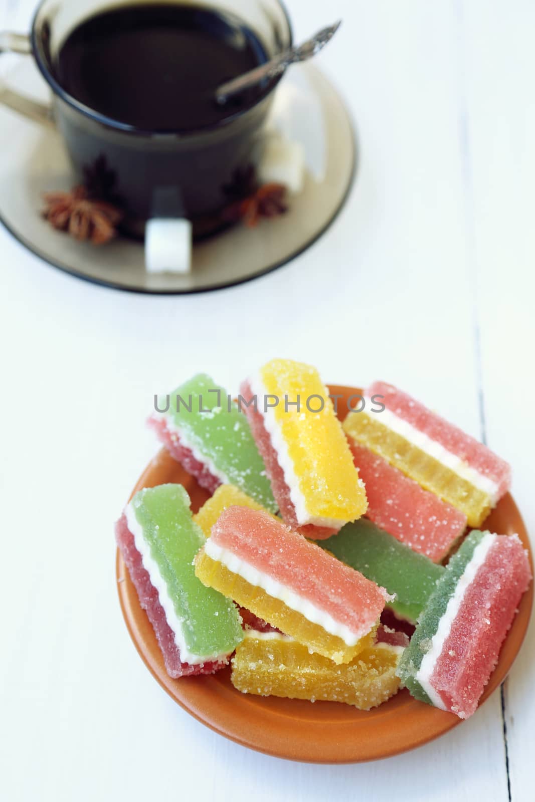 fruit jellies are in a saucer, near a cup with tea
