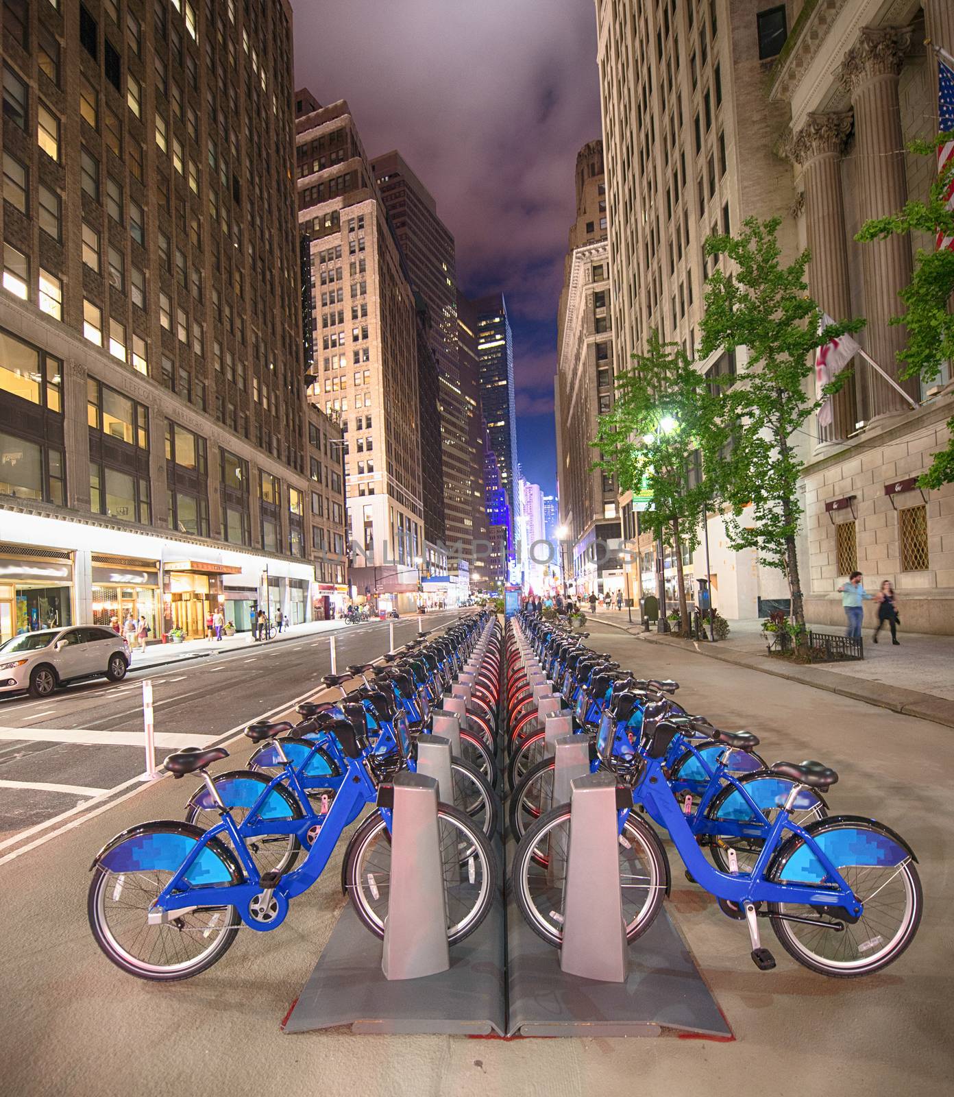 A row of blue bicycles on New York street at night by jovannig
