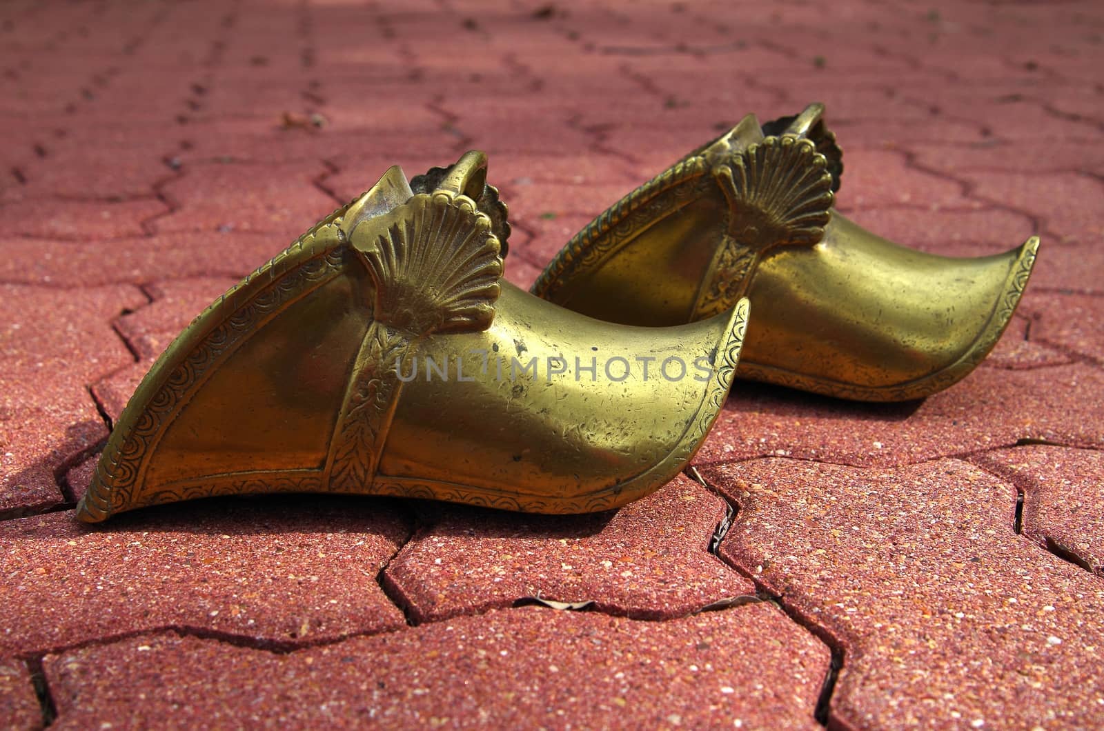 A pair of gold gaucho stirrups against a brick walk