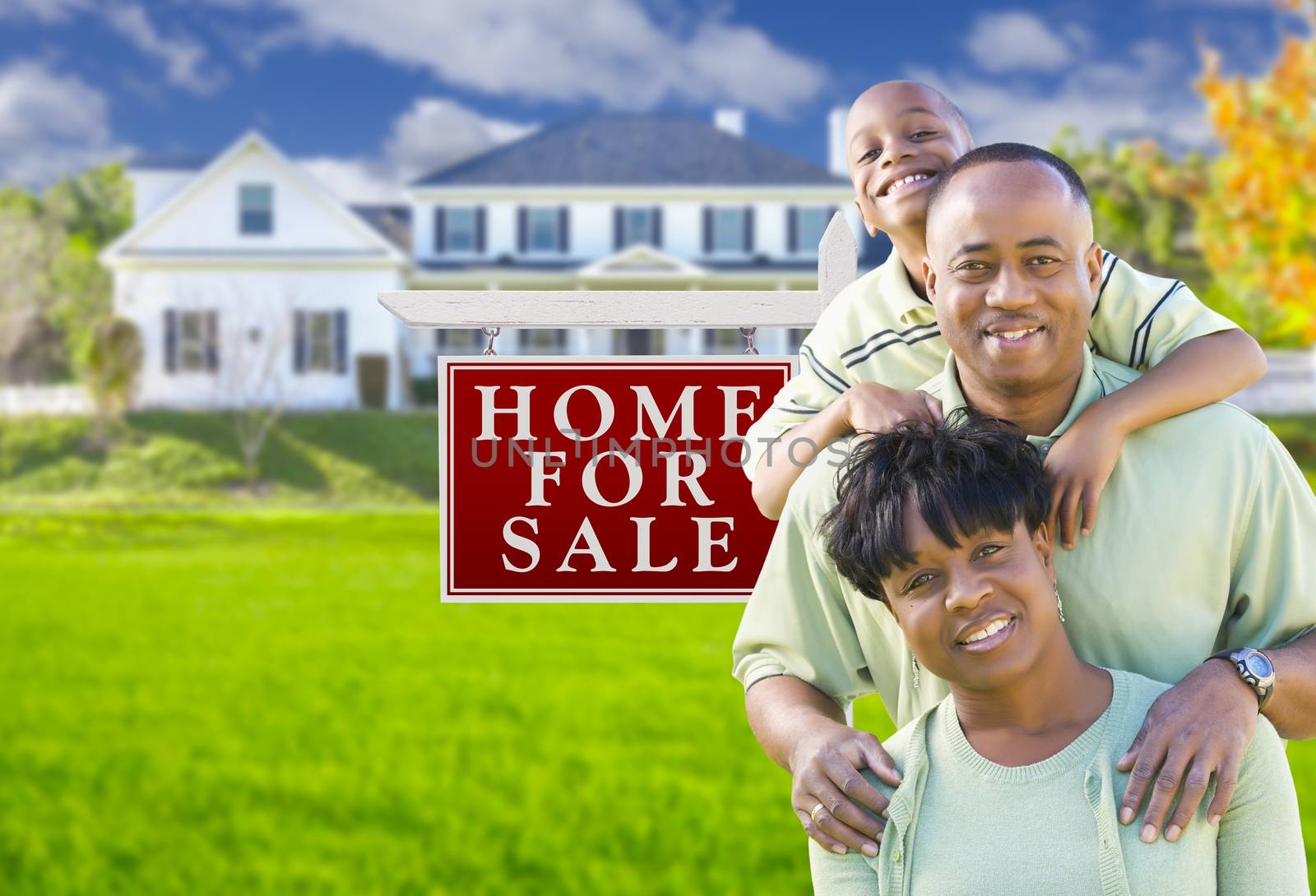 Happy African American Family In Front of For Sale Real Estate Sign and House.
