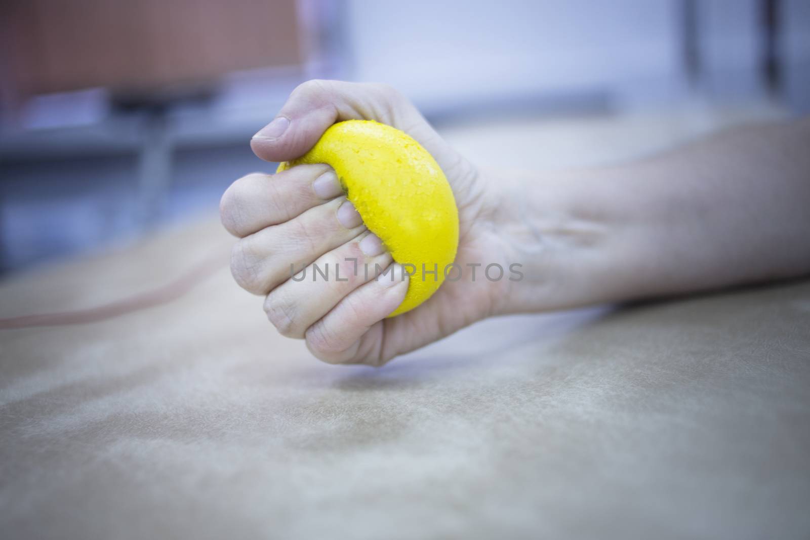 Female patient with physical injury and Rheumatoid arthritis squeezing physiotherapy ball with hand in hospital clinic resting on bed.