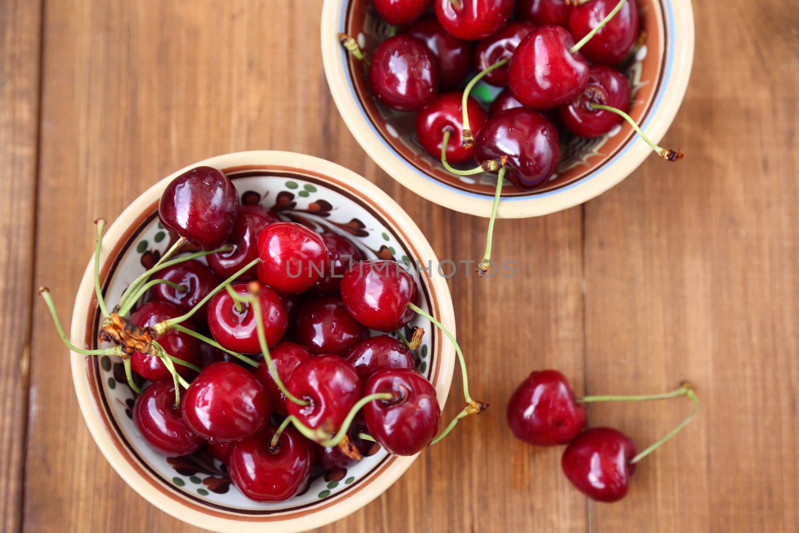 many ripe raw wet sweet cherry in dish on wooden background