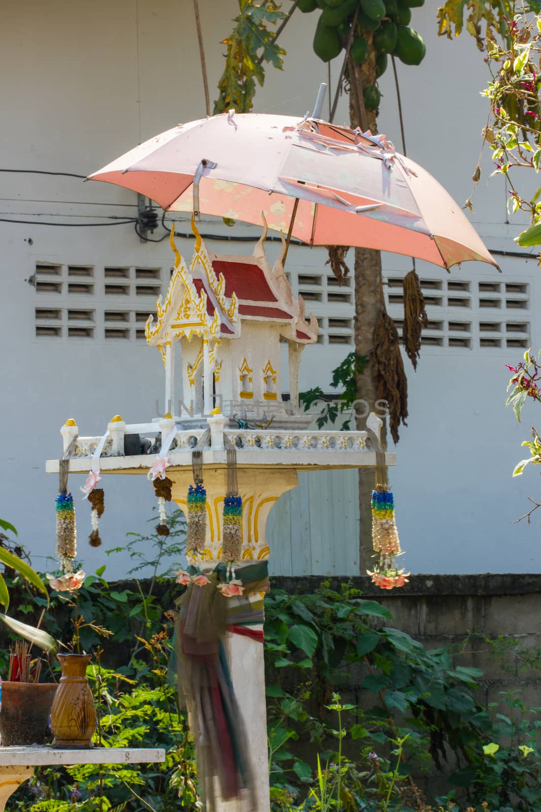 white spirit house in thailand with old umbrella over it