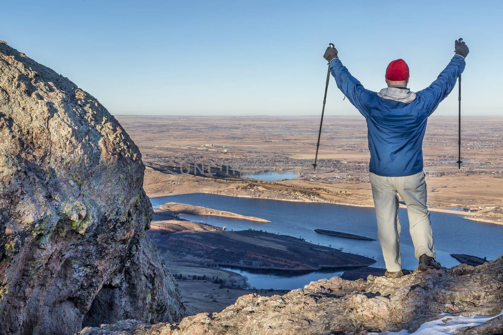 a male hiker with trekking poles overlooking Horsetooth Reservoir from Arthur's Rock near Fort Collins, Colorado, a typical winter scenery without snow