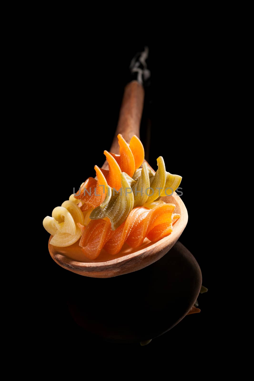 Fusilli on wooden spoon isolated on black background. Culinary pasta cooking background.