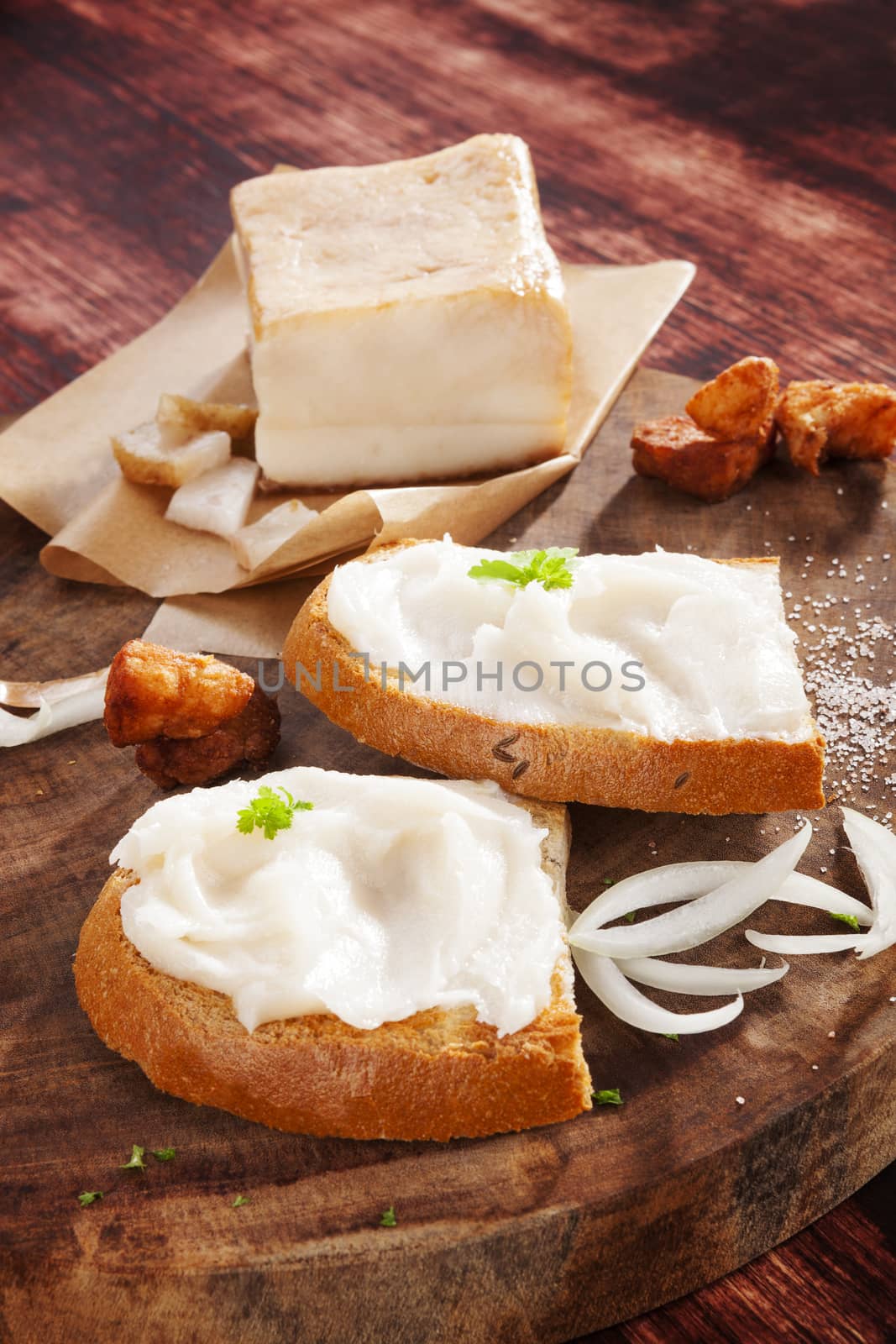 Bread slices with lard, pork scratchings and bacon on wooden cutting board on brown background. Traditional culinary eating. 