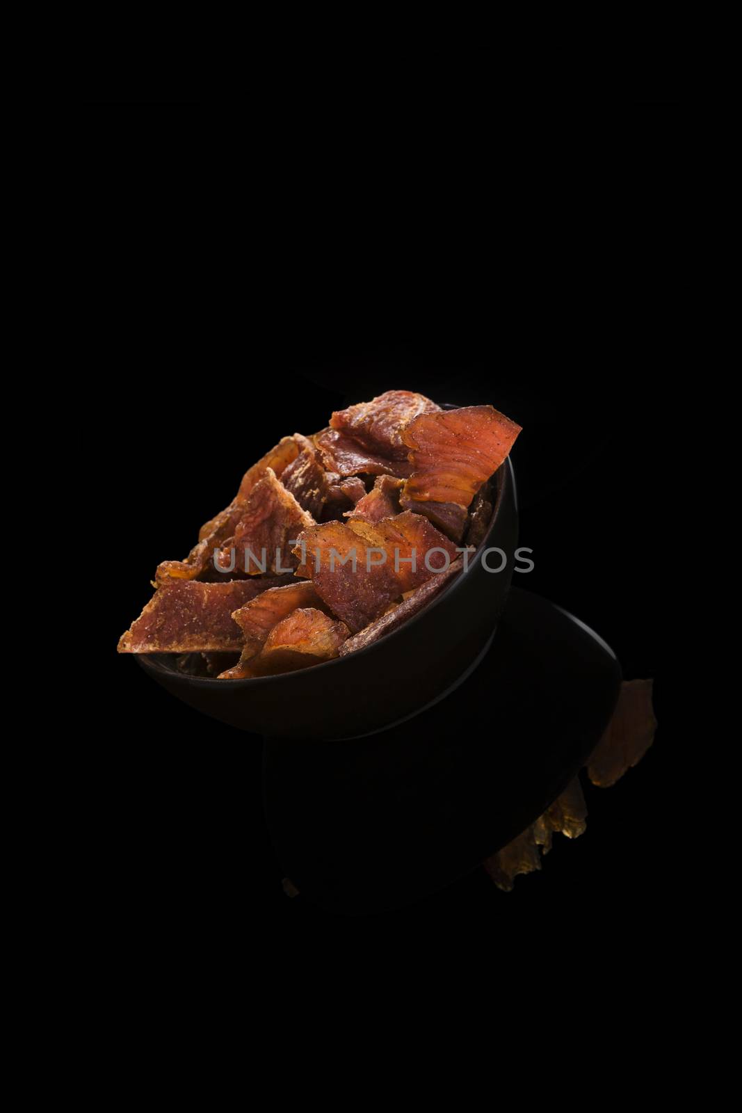 Beef jerky, preserved dry meat in black bowl isolated on black background. Culinary meat eating.