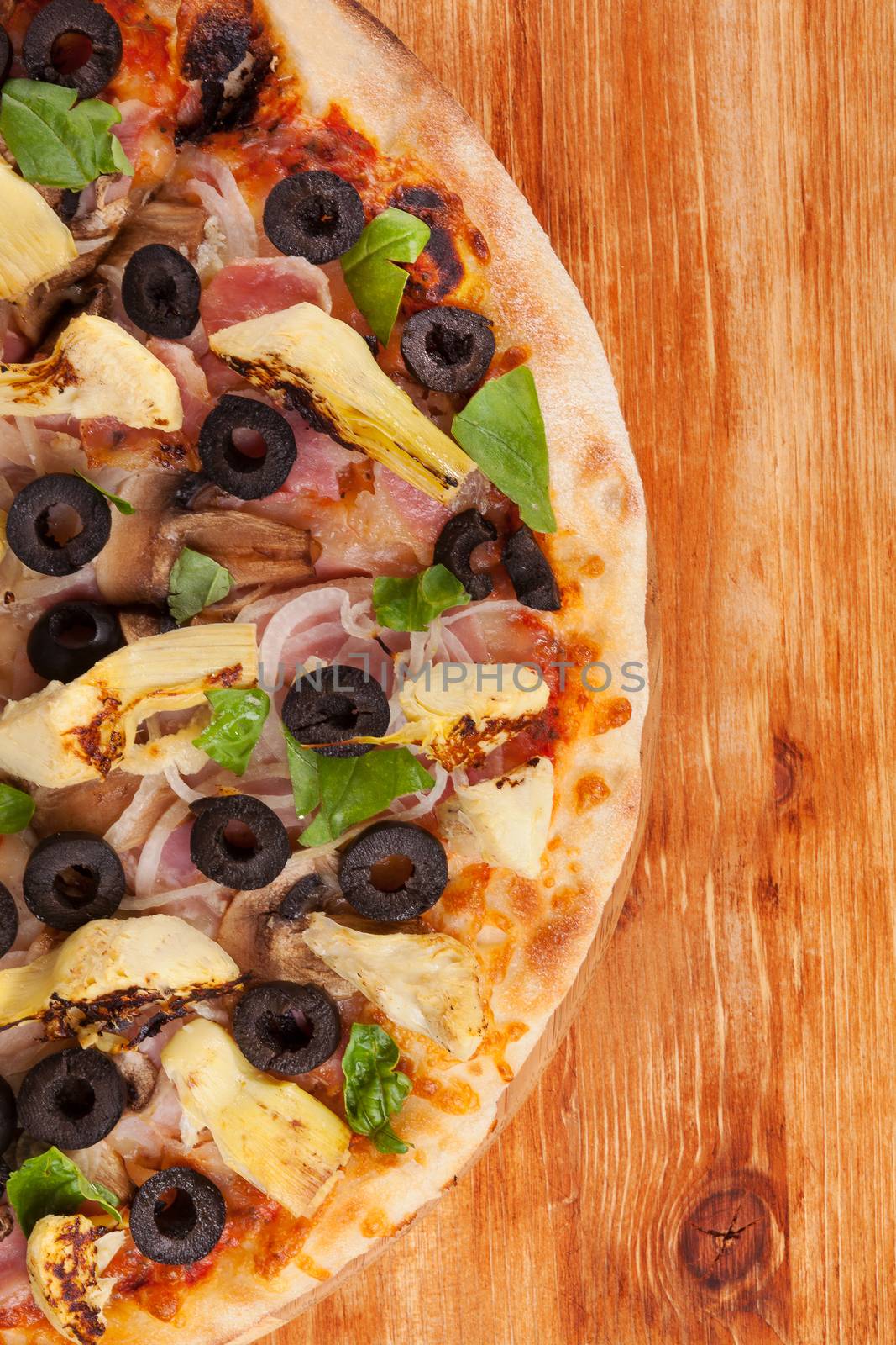 Delicious colorful pizza with tomatoes, melted cheese, black olives, onions, ham and fresh herbs on brown wooden background. Culinary mediterranean pizza eating.