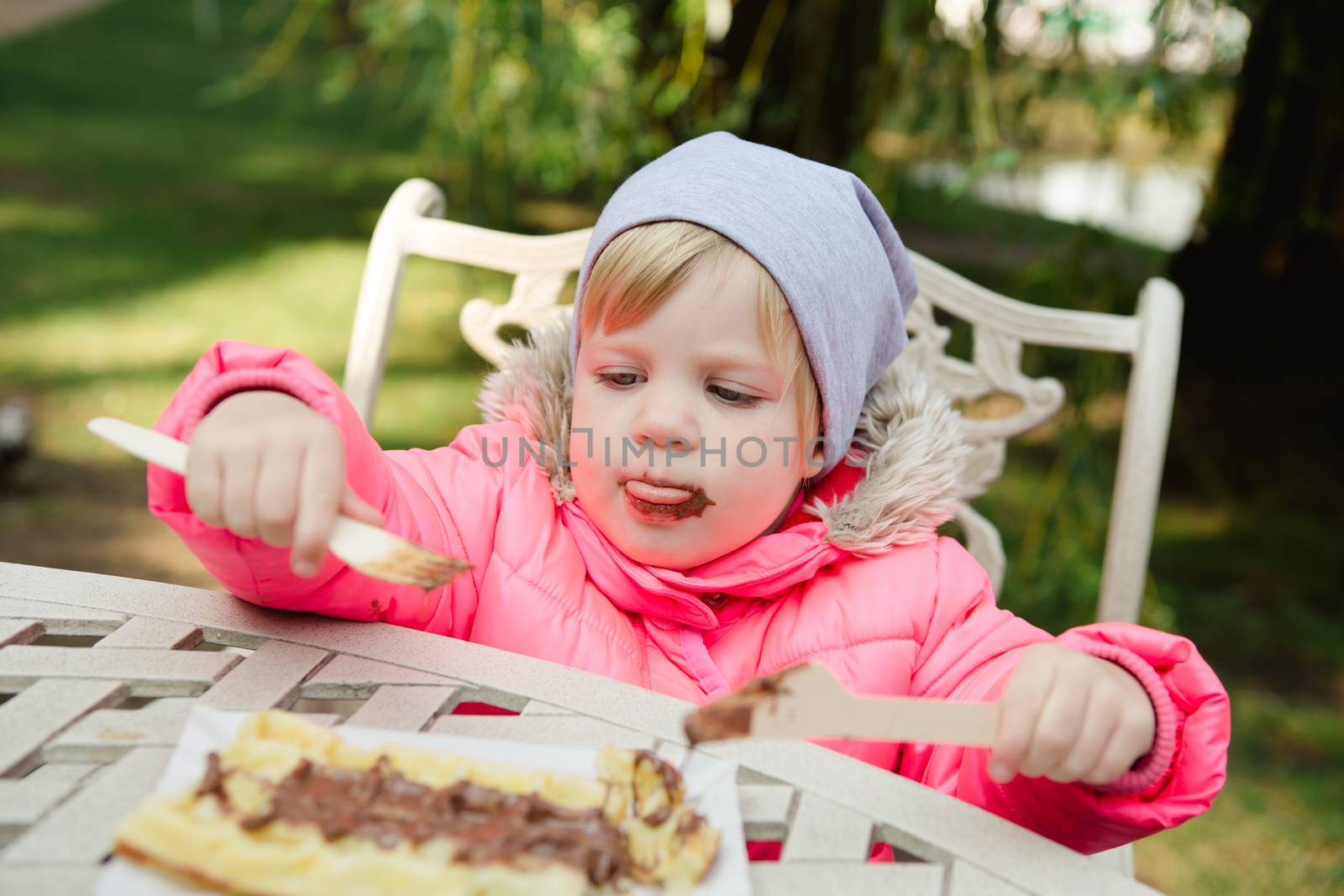 Child eating waffles with chocolate in a spring park