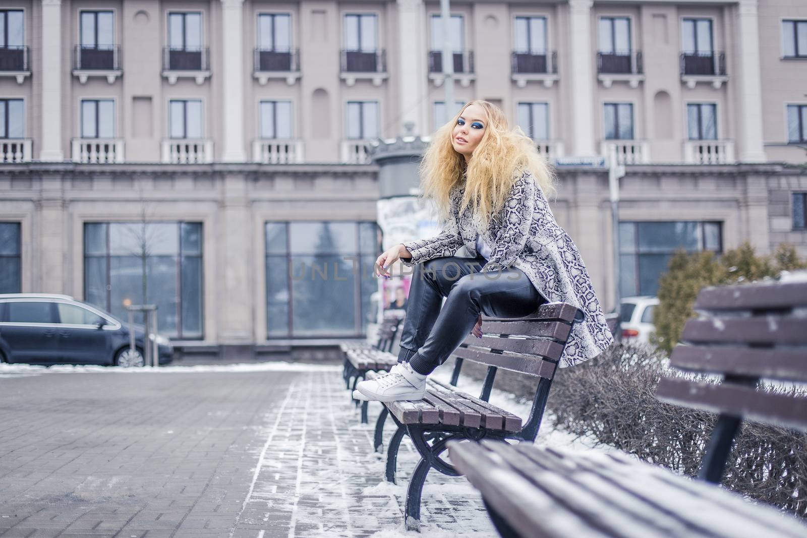 Stylish young girl in leather pants is sitting on a bench