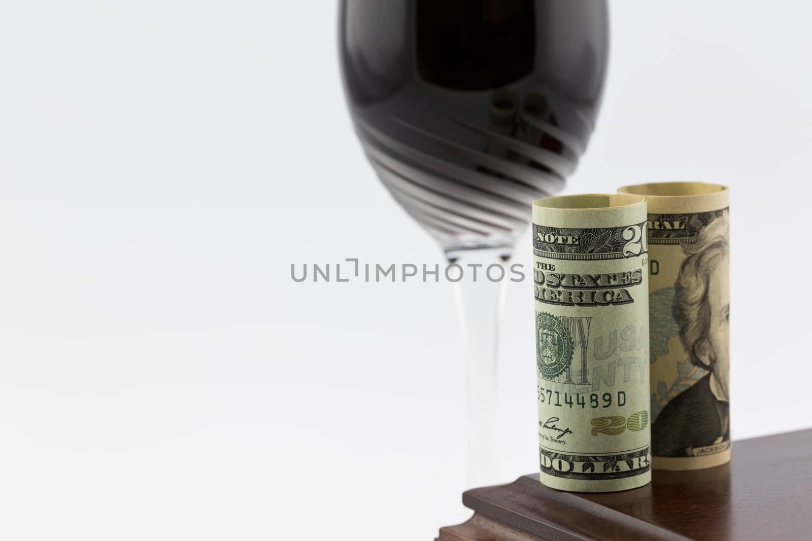 American currency placed on polished wood box in front of stem glass with red wine; horizontal image with white copy space; 