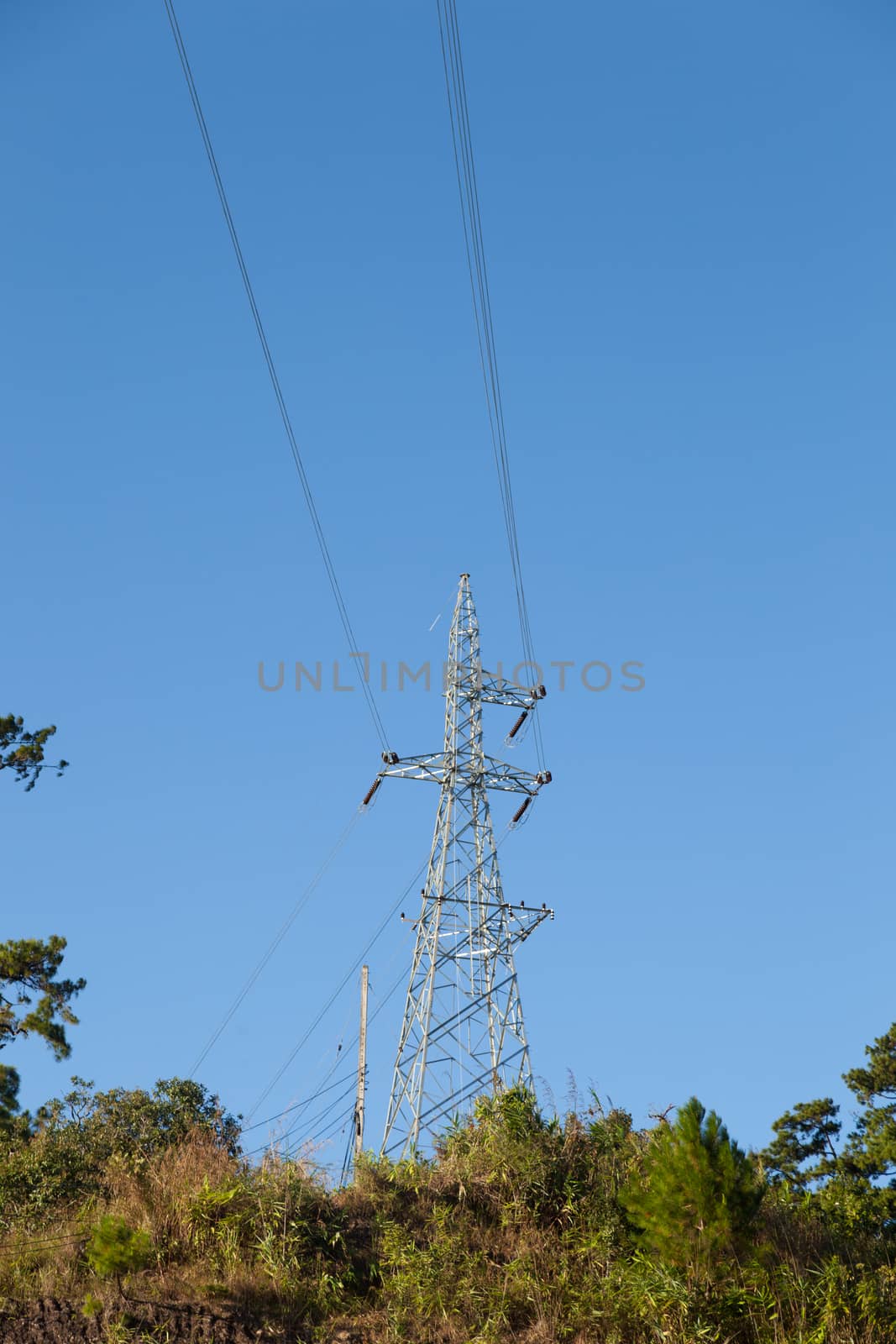 High voltage pylons. On a mountain with trees. Cloudy and clear sky.