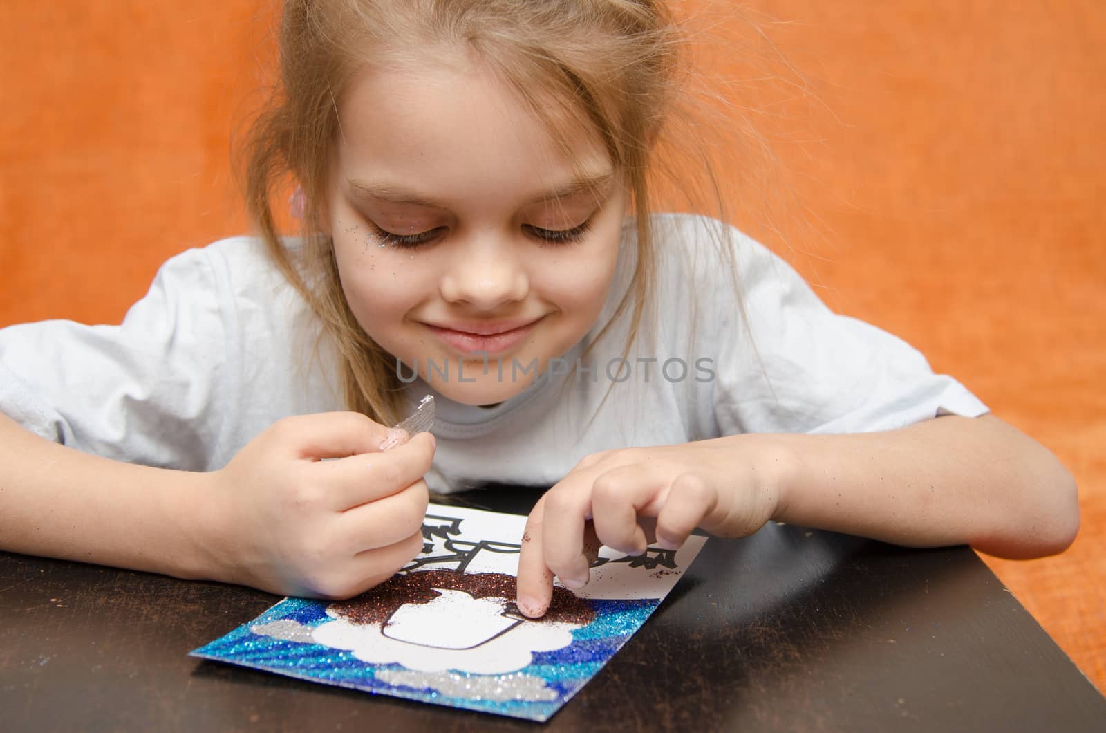 five year old girl sitting at the table and collects sand applique