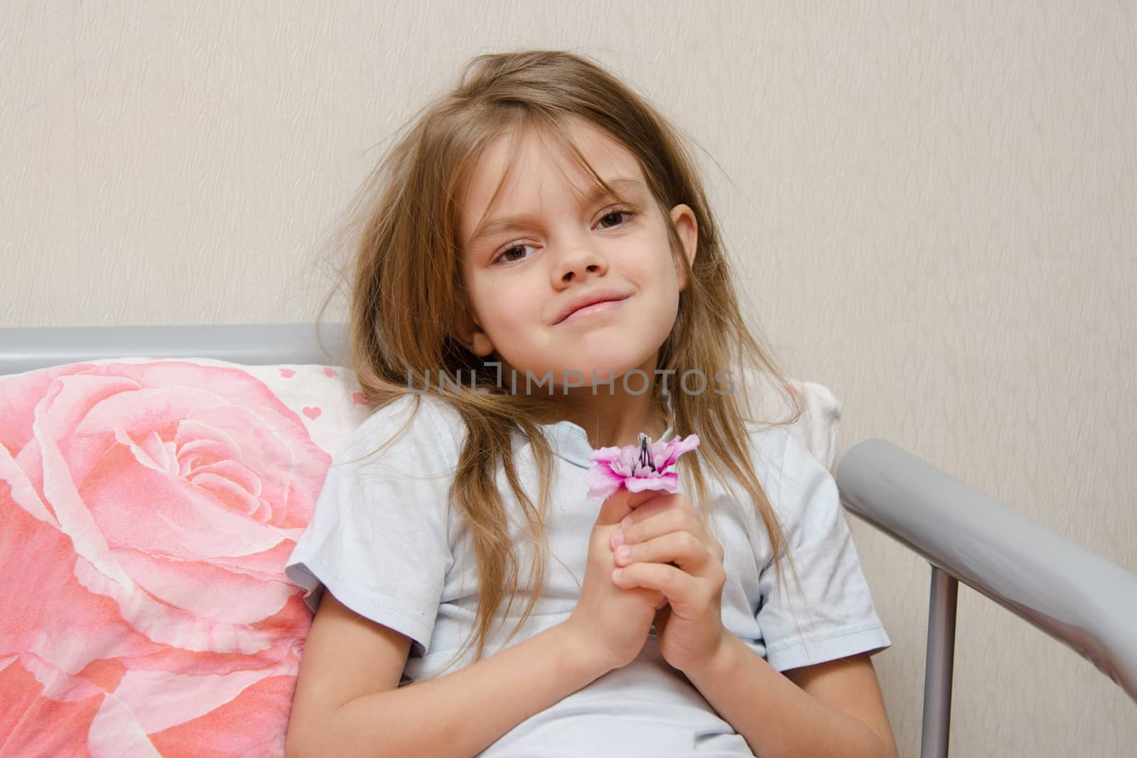 Touching five year old girl sitting in bed with a flower in hands