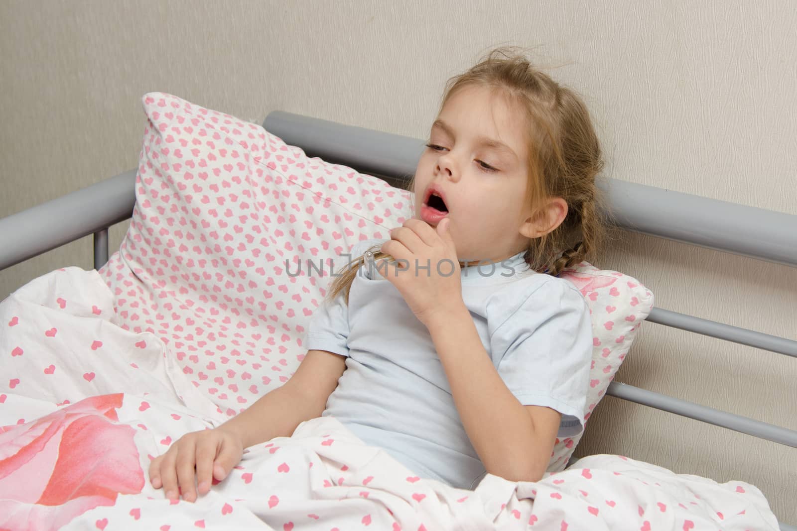 Six year old girl coughs diseased lying in bed with a thermometer on the mouse