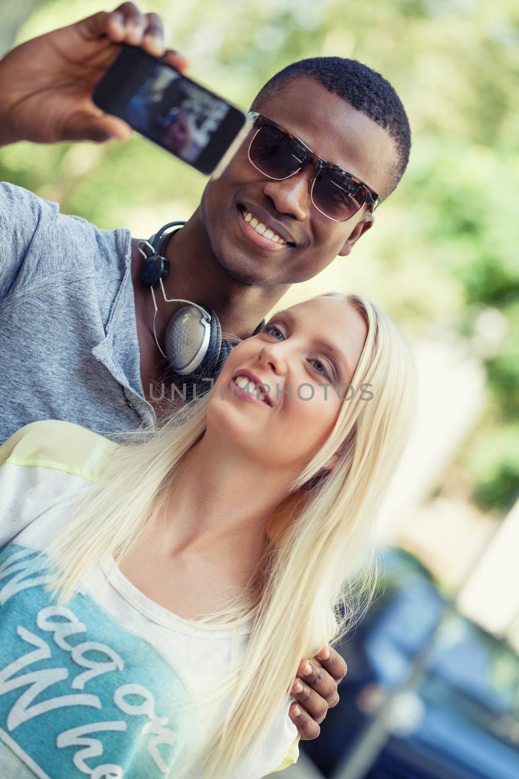 young smiling multiracial couple taking foto by smartphone outdoor in summer