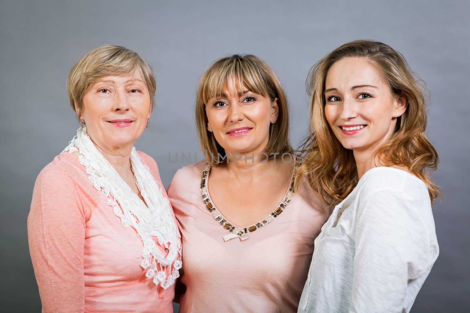 Three generations of attractive women with blond hair and a striking family resemblance posing together arm in arm looking at the camera with friendly smiles