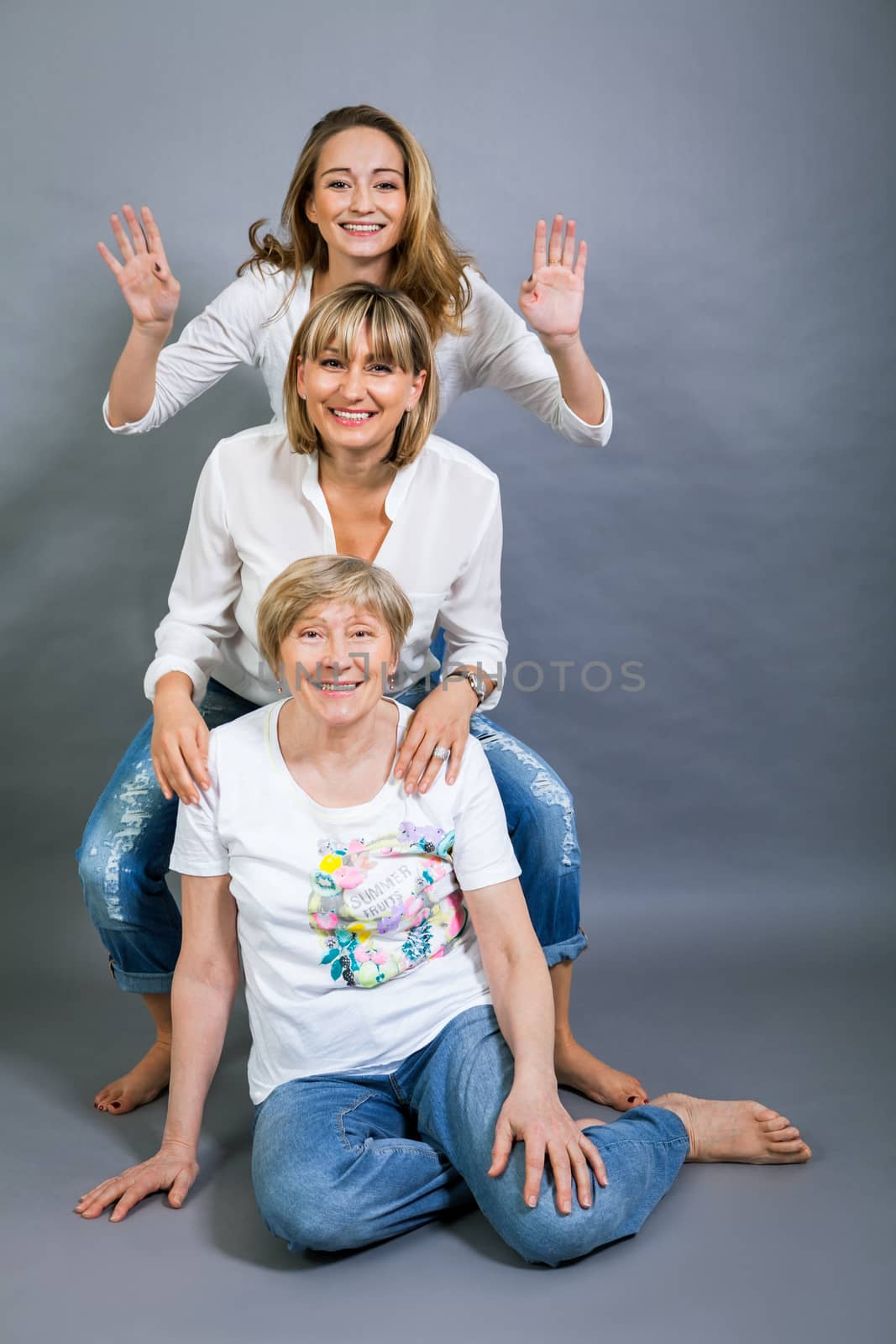 Three generations of attractive women with blond hair and a striking family resemblance posing together arm in arm looking at the camera with friendly smiles